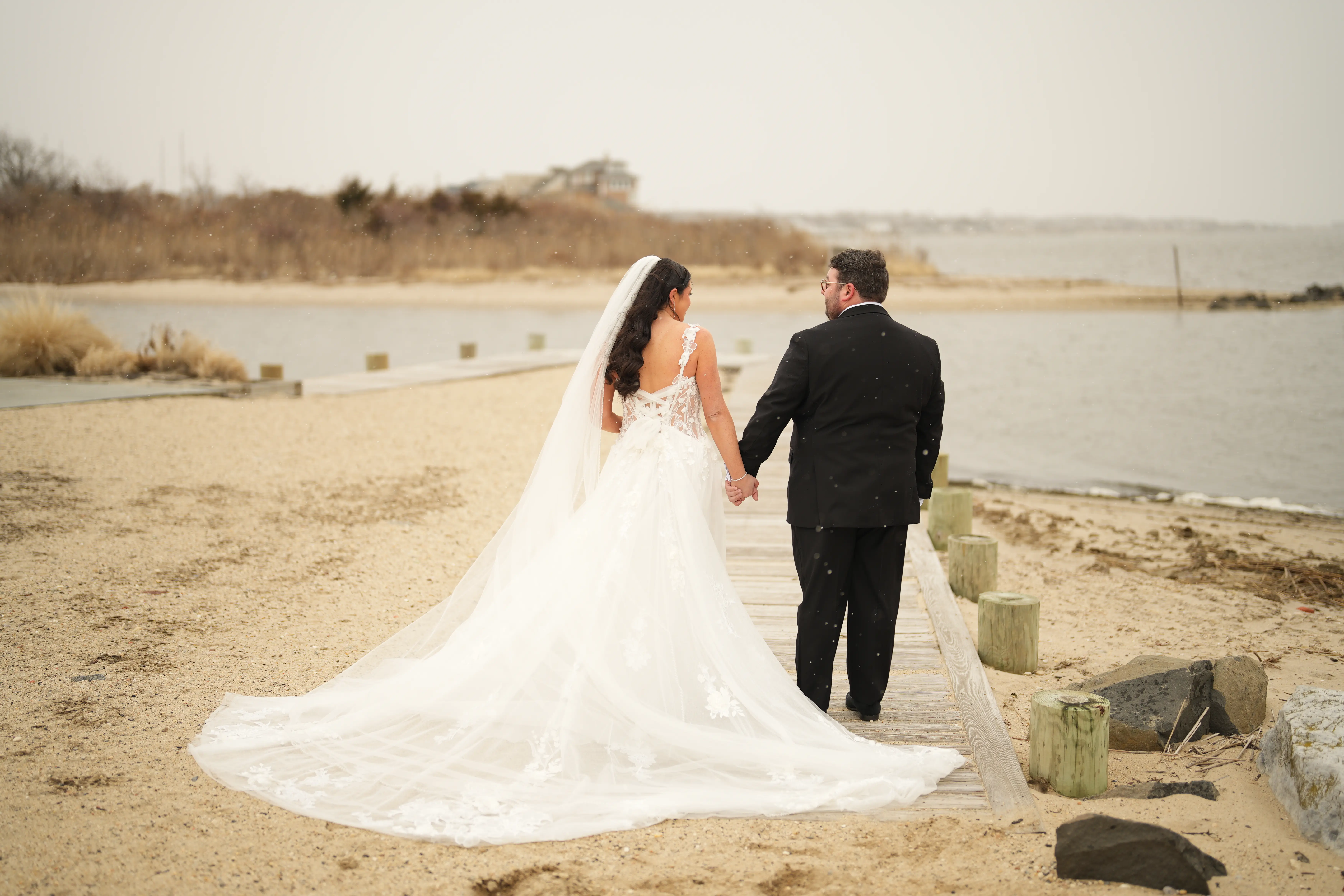 Bride Wearing Morwenna Wedding Dress By Maggie Sottero Holding Hands With Groom On A Beach