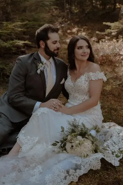 Bride with groom wearing romantic lace off-the-shoulder wedding dress outside in the mountains.
