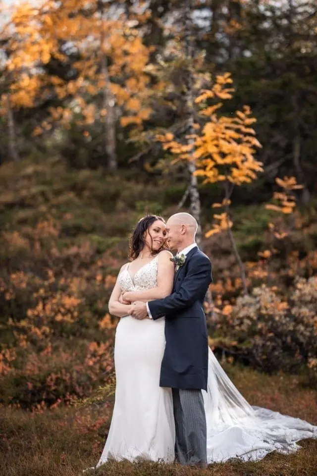 Bride and groom hugging with Fall or Autumn trees in background.