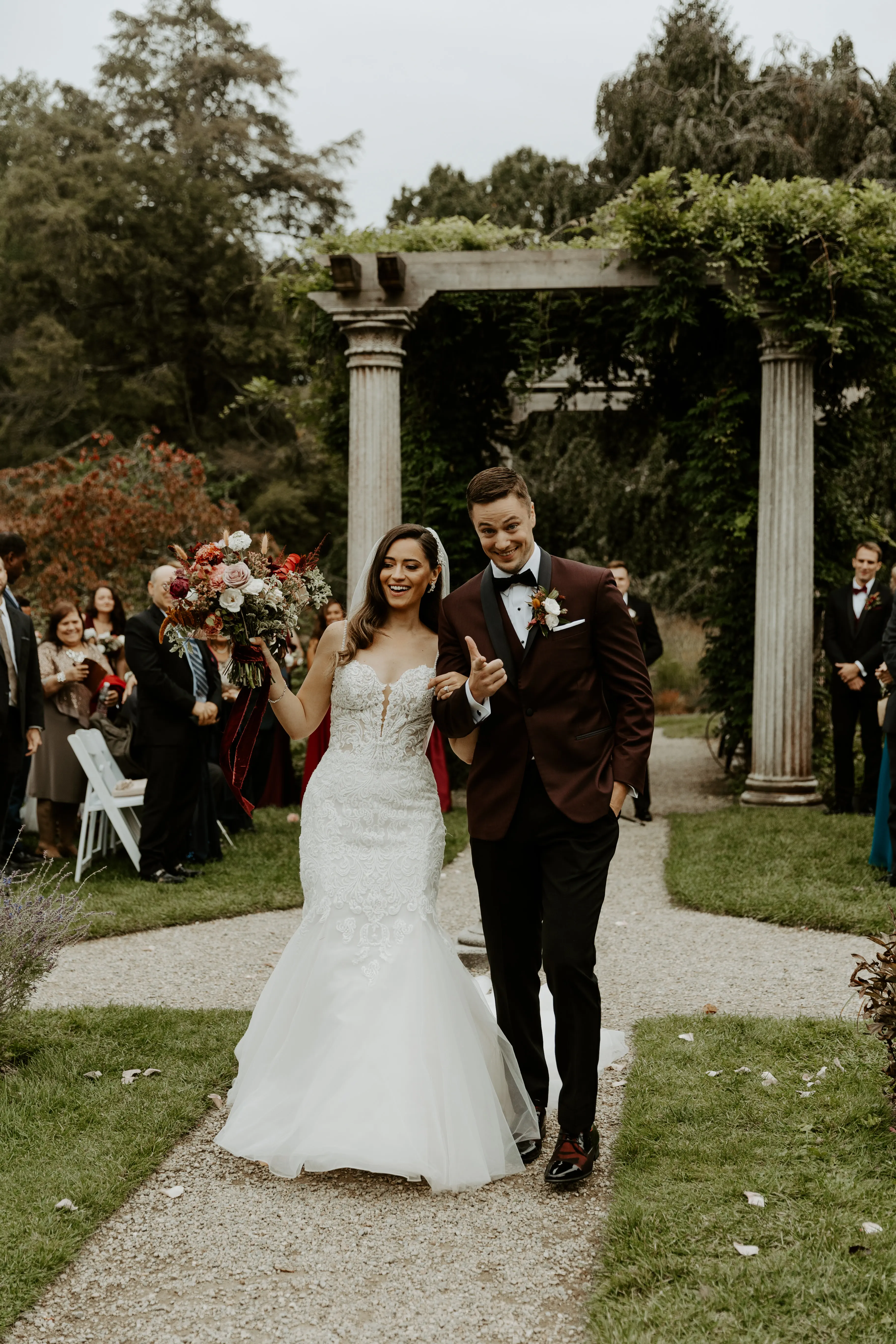 Bride with groom wearing lace fit-and-flare wedding dress holding bridal bouquet outdoors.