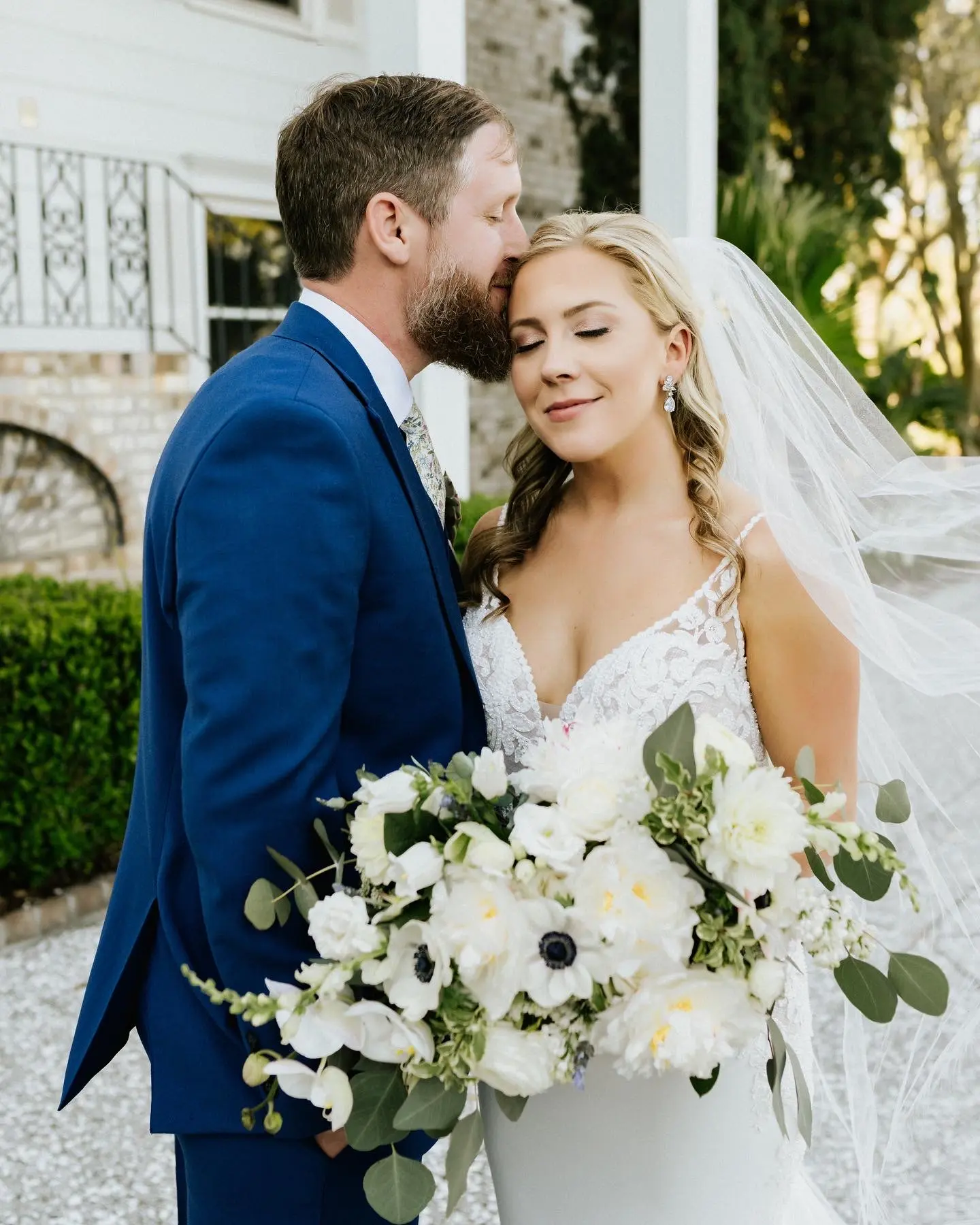 Groom Kisses Bride In A Sleek Lace Spaghetti Strap Fit and Flare Wedding Dress Named Nikki By Maggie Sottero With Flower Bouquet