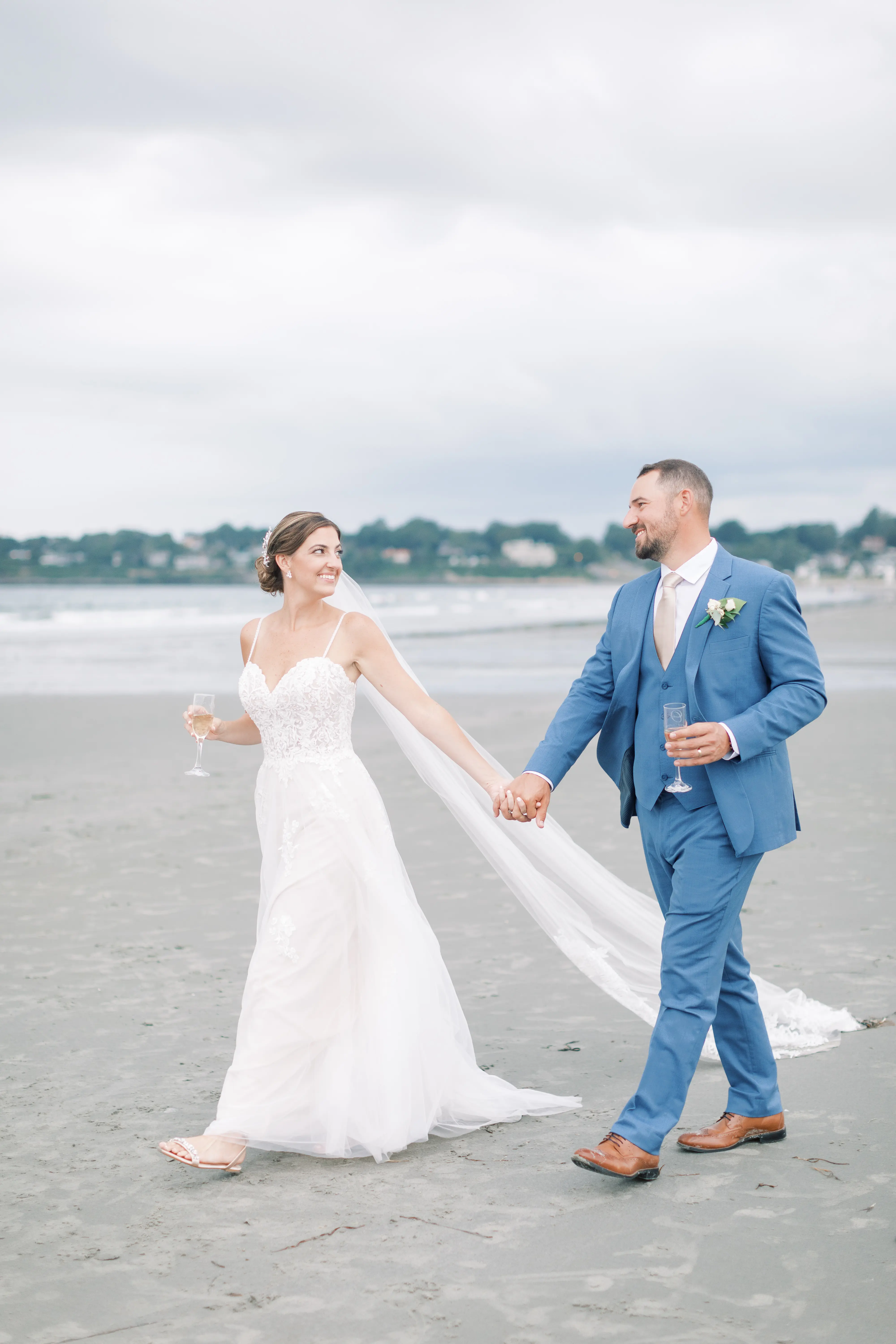 Bride Wearing Boho Sheath Wedding Dress Called Marisol By Rebecca Ingram Walking On The Beach With Groom