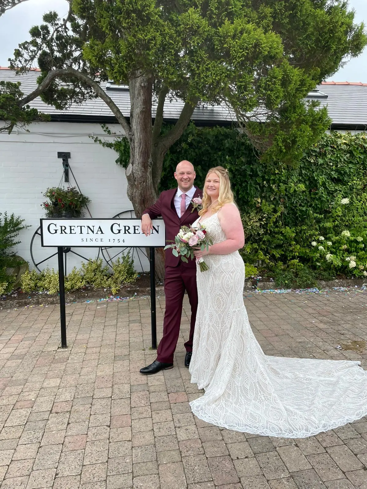 Bride wearing wedding dress called Daxton stood with groom next to Gretna Green sign.
