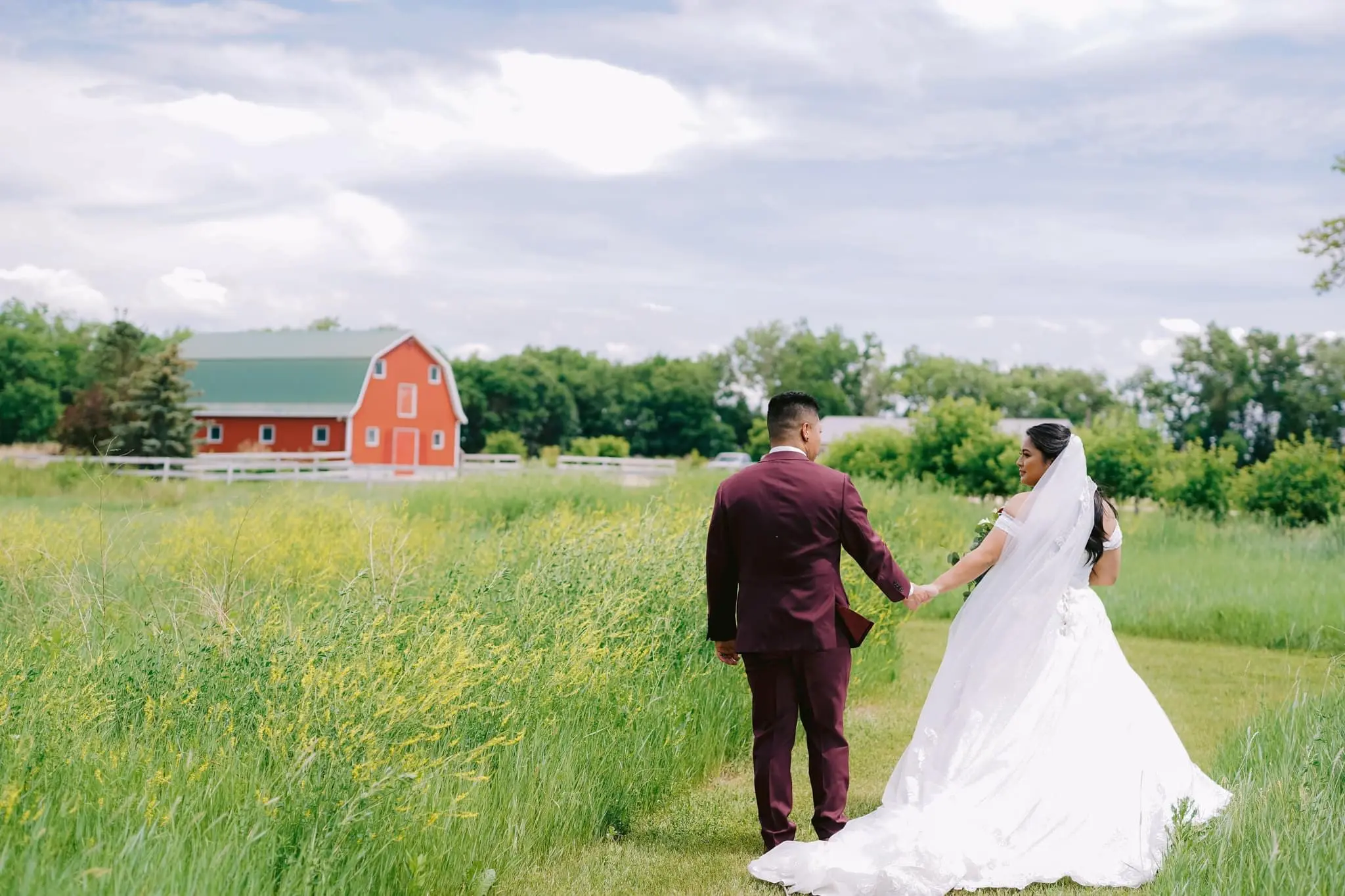 Bride and groom walking through a field.