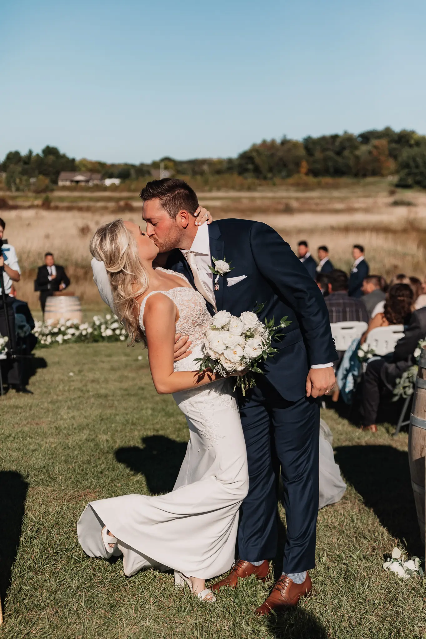 Newlyweds kissing in the aisle at their sunny outdoor wedding.