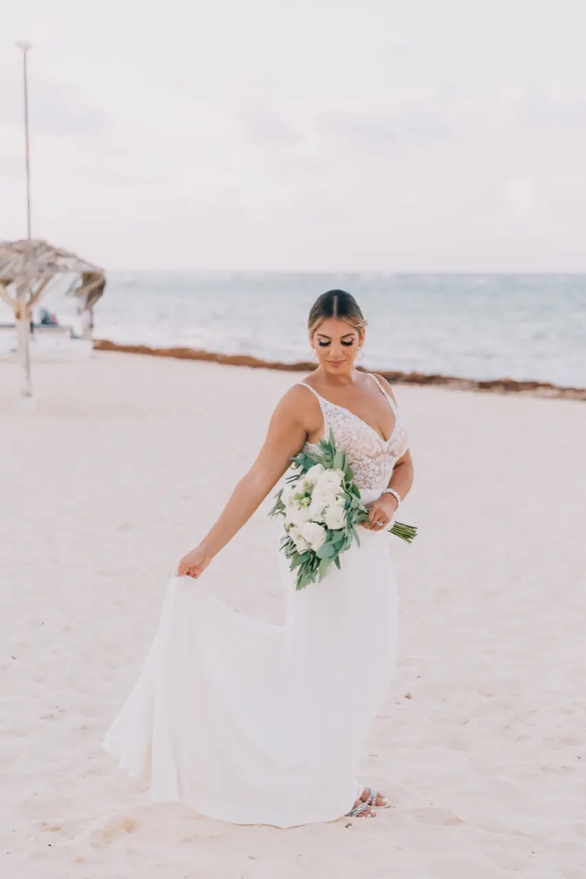 Bride standing in the sand holding her train wearing wedding dress called Carmen.