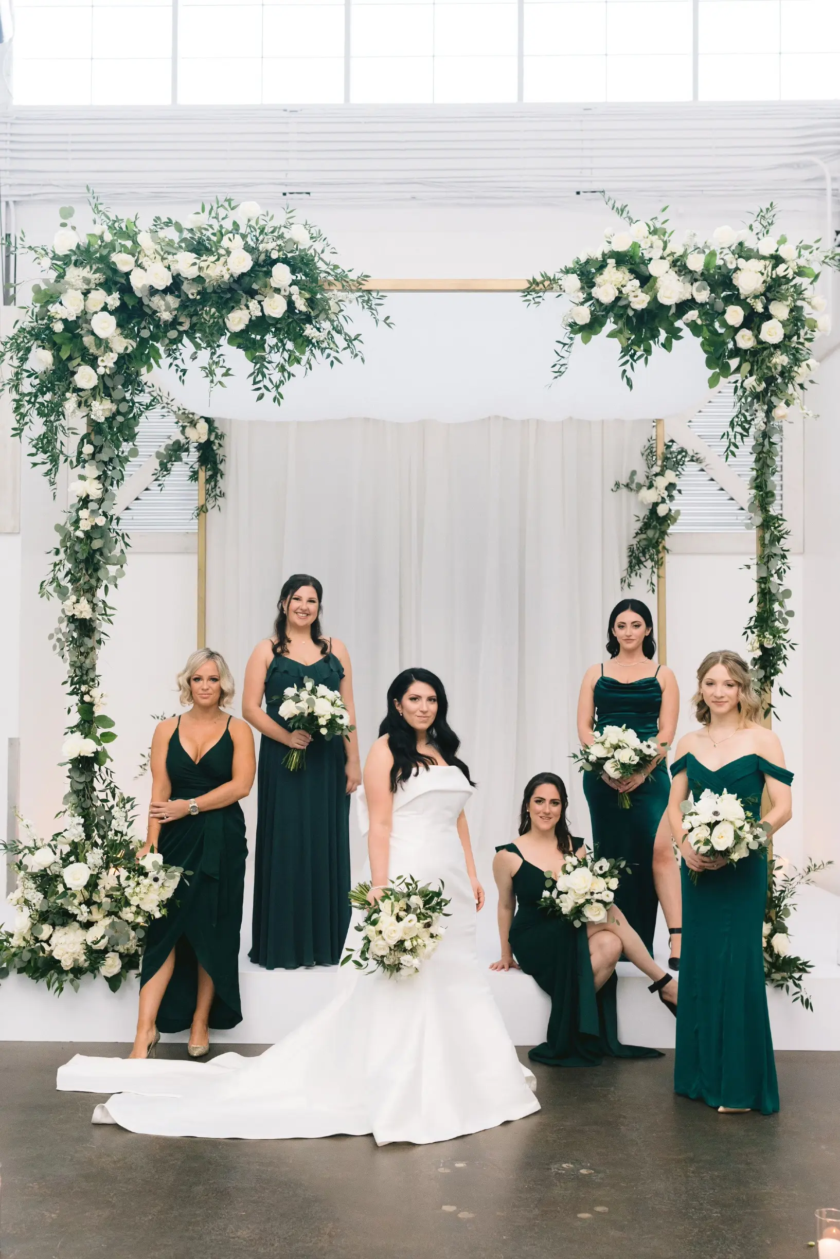 Bride with bridesmaids wearing strapless satin mermaid wedding dress with big bow on the back.