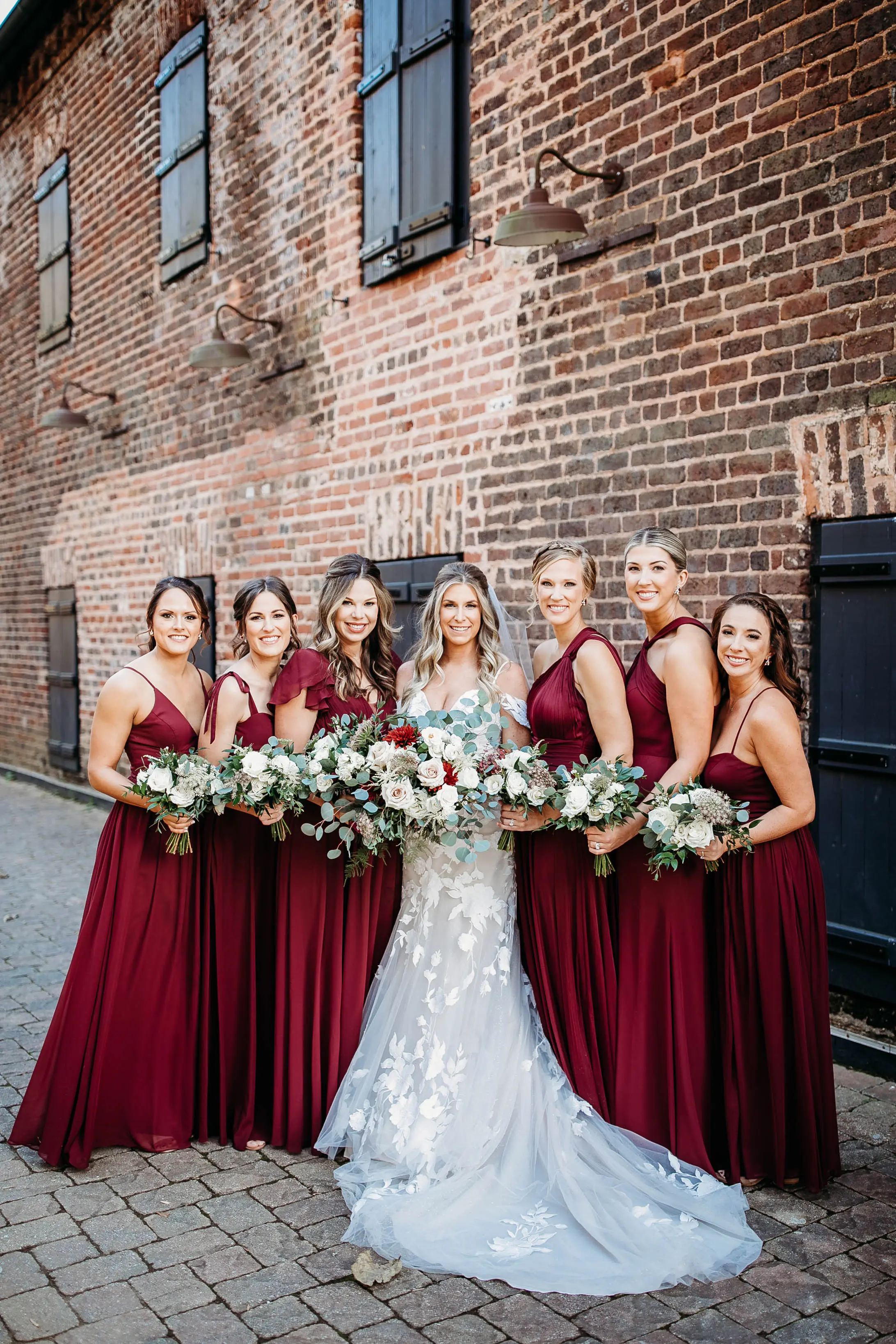 Bride Standing With Bridesmaids. Bride Wearing Mermaid Wedding Dress With Oversized Lace Called Hattie By Rebecca Ingram