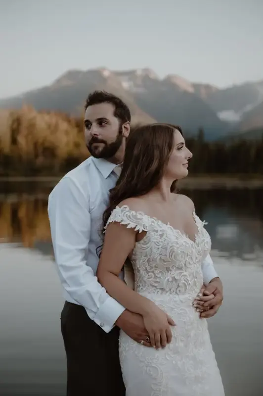 Bride with groom wearing romantic lace off-the-shoulder wedding dress outside in the mountains.