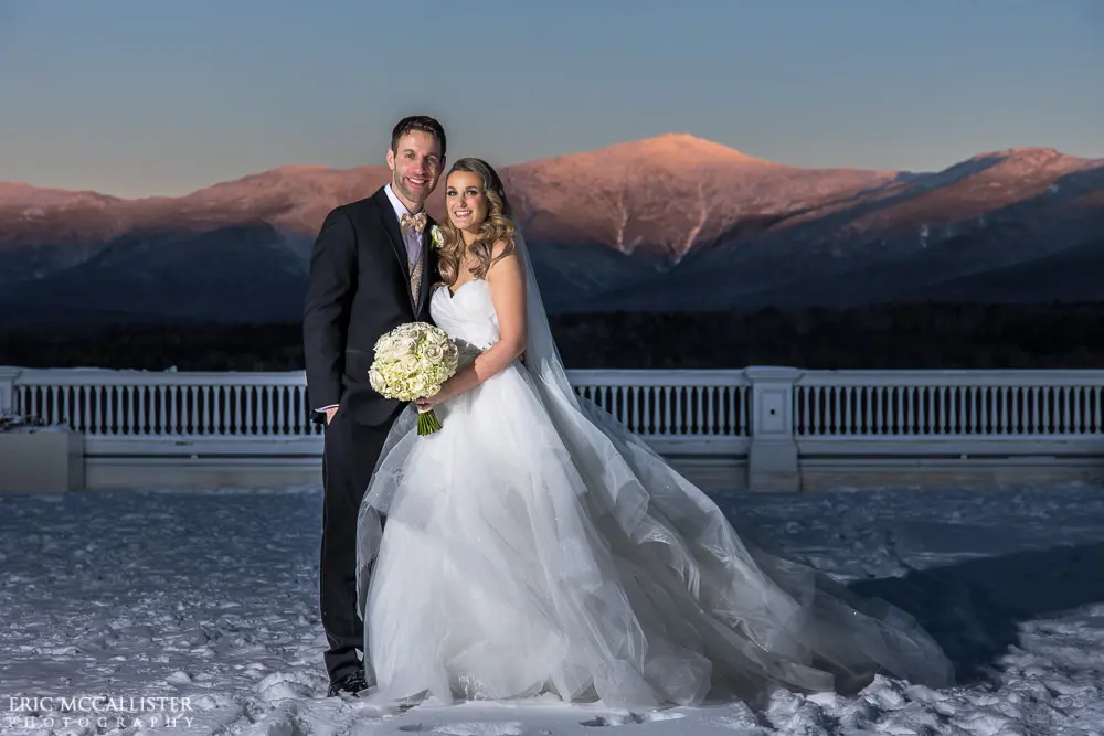 Bride with groom wearing strapless ballgown tulle wedding dress with sweetheart neckline outdoors in front of mountains.