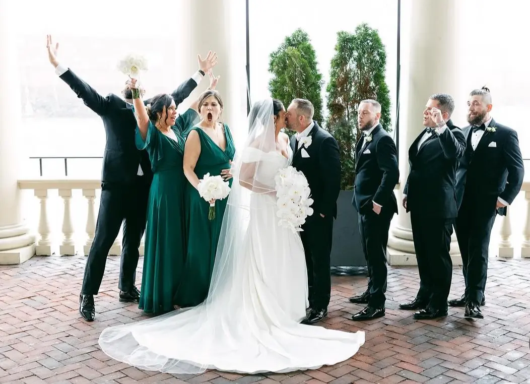 Bride wearing Ekaterina by Maggie Sottero kissing her husband in front of their wedding party