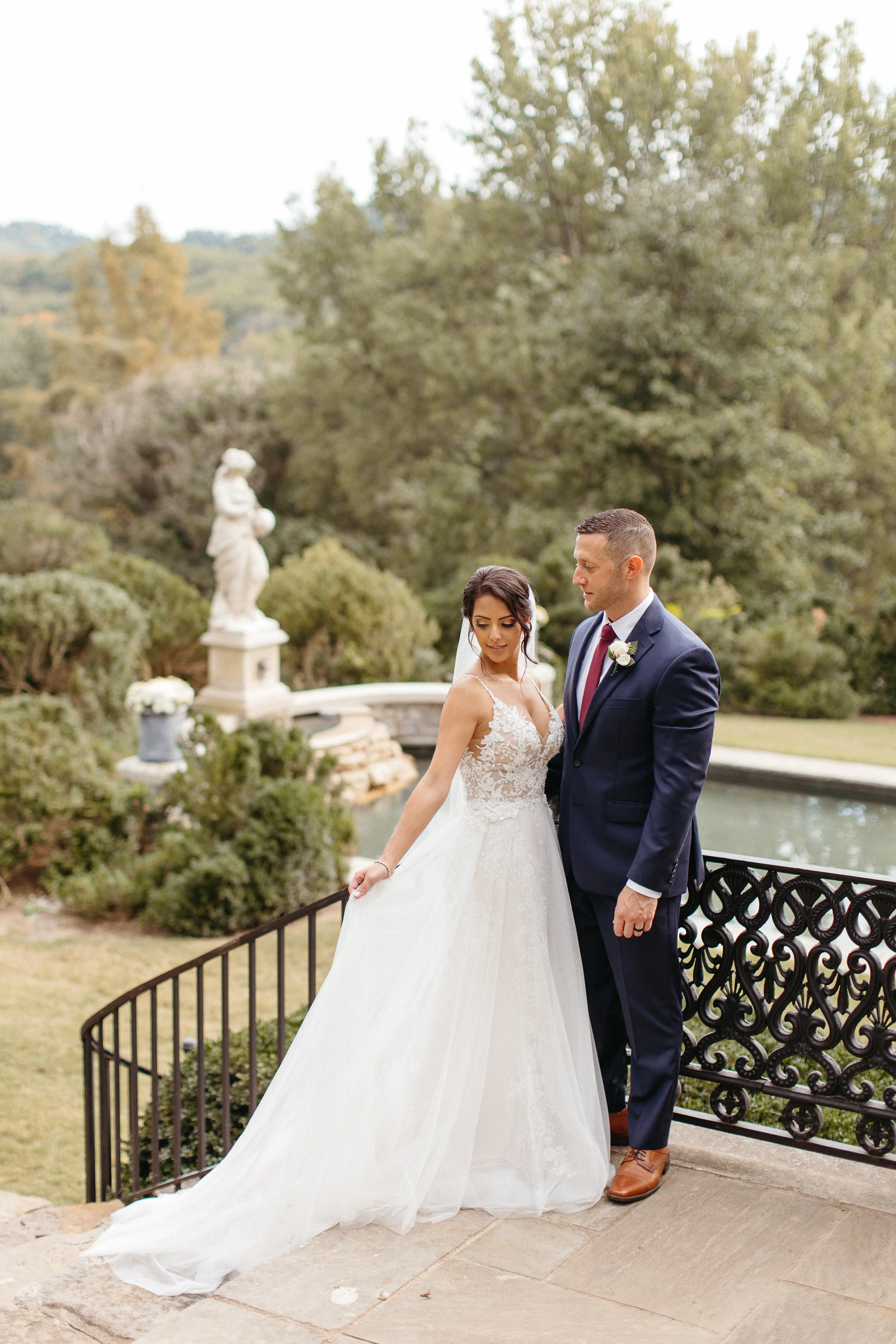 Groom looking at his bride as she arranges her train of wedding dress called Roanne Rose.