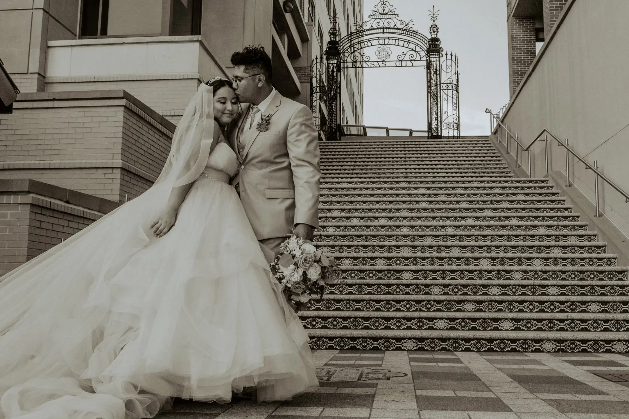 Bride Wearing Tiered Princess Skirt Wedding Dress Called Yasmin By Maggie Sottero With Groom In Front Of Stairs