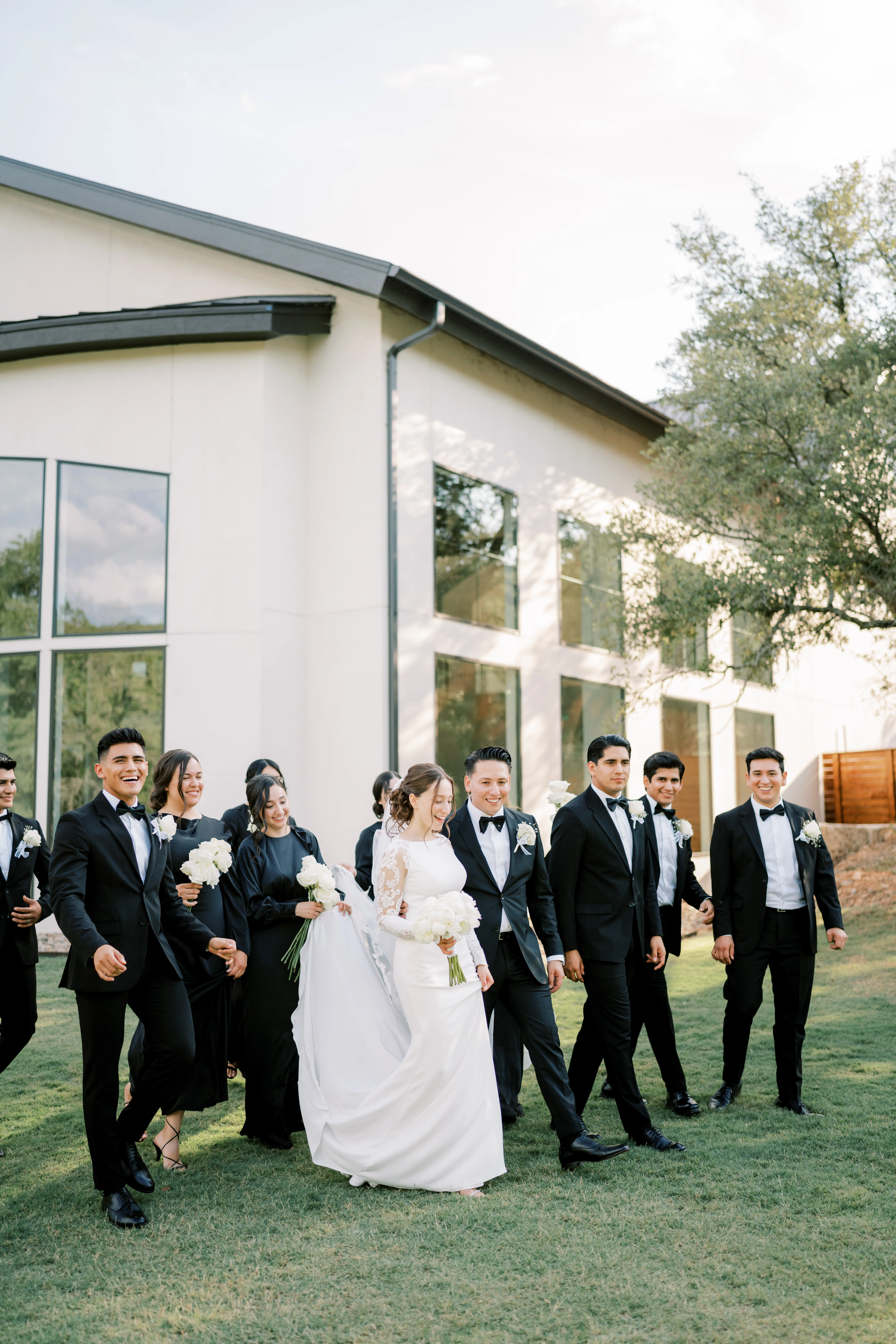 Bride Wearing Simple Long Sleeve Wedding Dress Called Bethany By Rebecca Ingram Walking Outside With Groom And Bridal Party