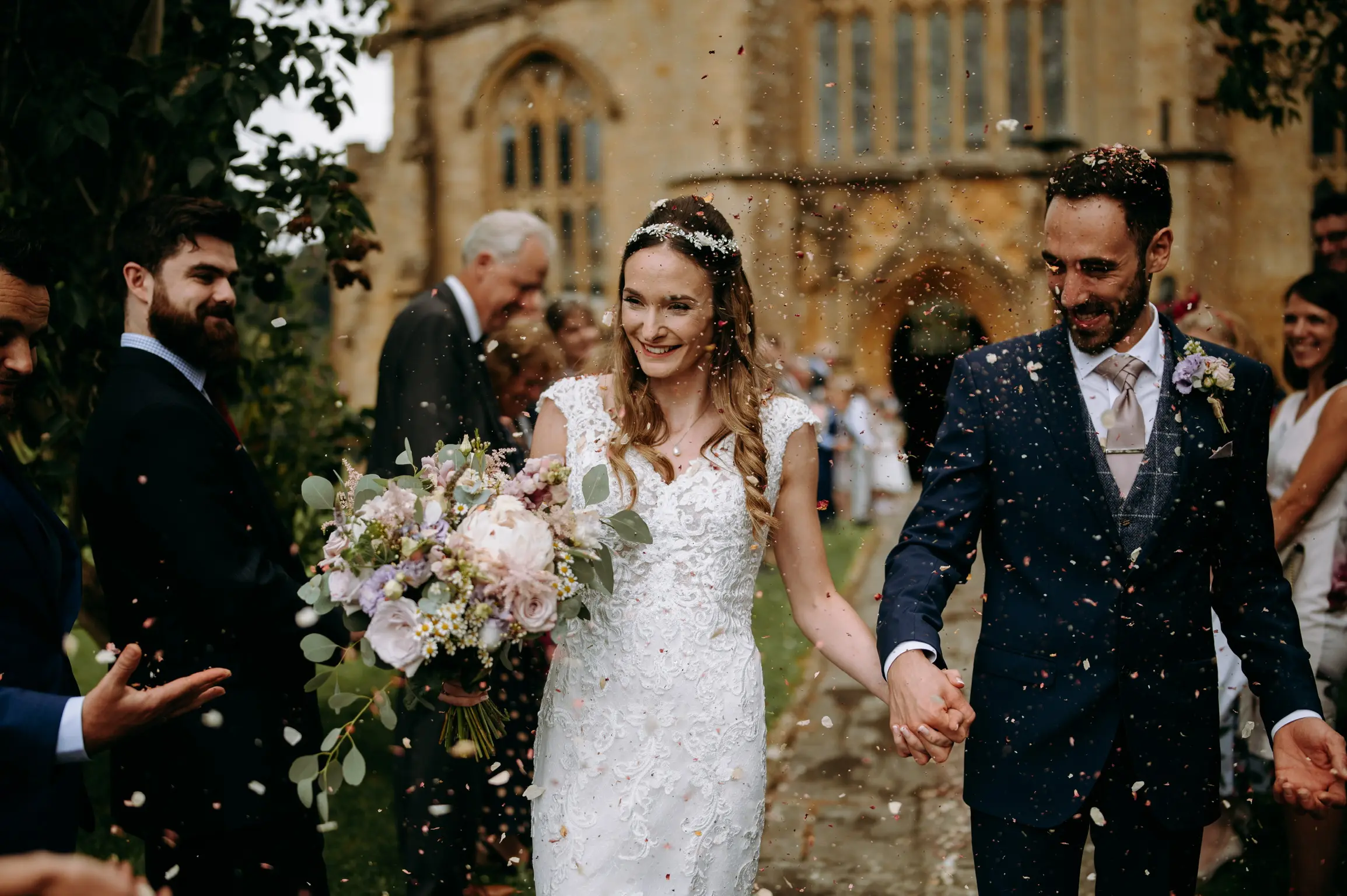 Confetti throw with bride holding mixed pastel colored bouquet holding grooms hand.