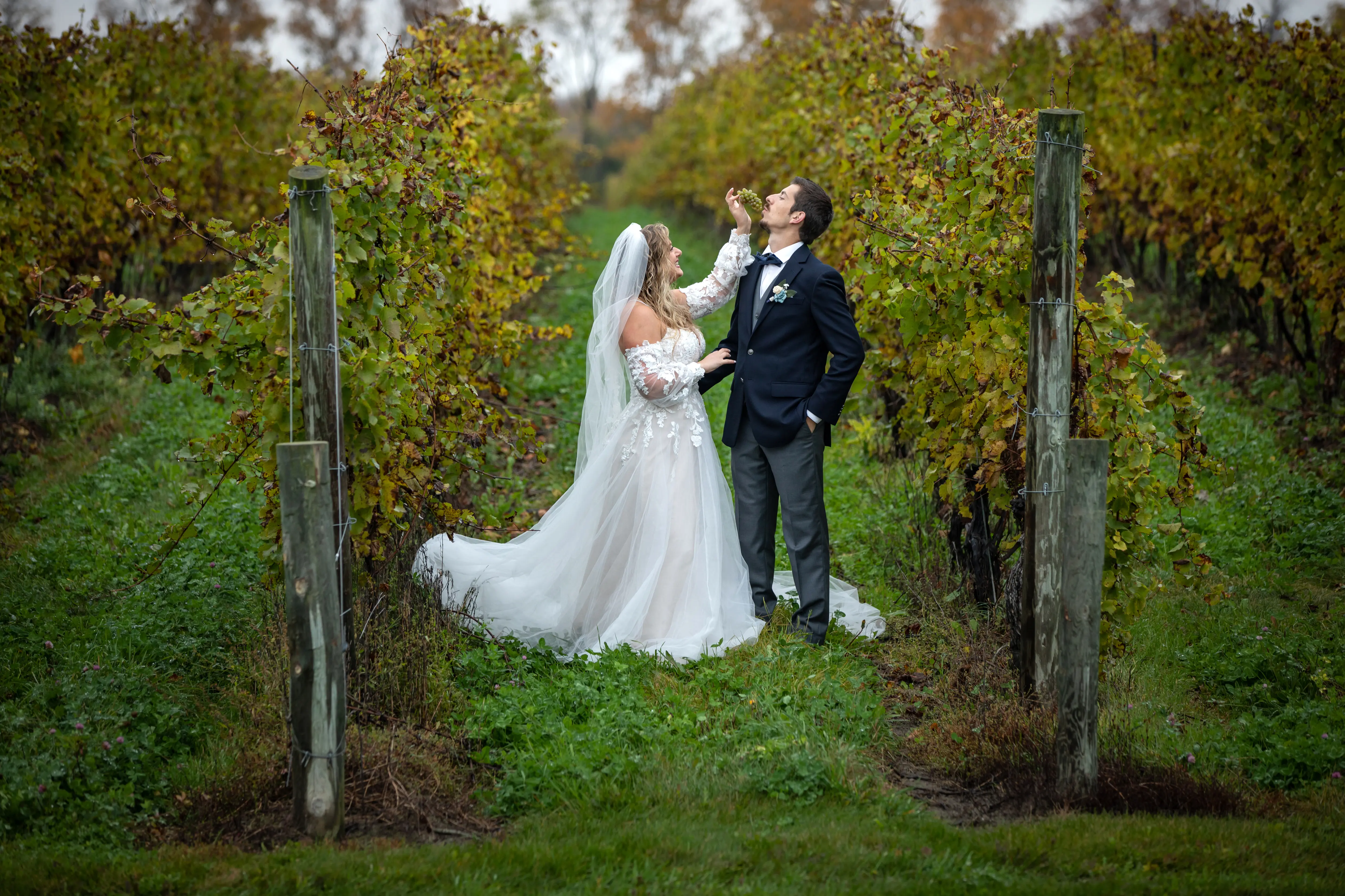 Bride Wearing Boho A-Line Wedding Dress Called Stevie By Maggie Sottero Feeding The Groom Grapes In A Vineyard