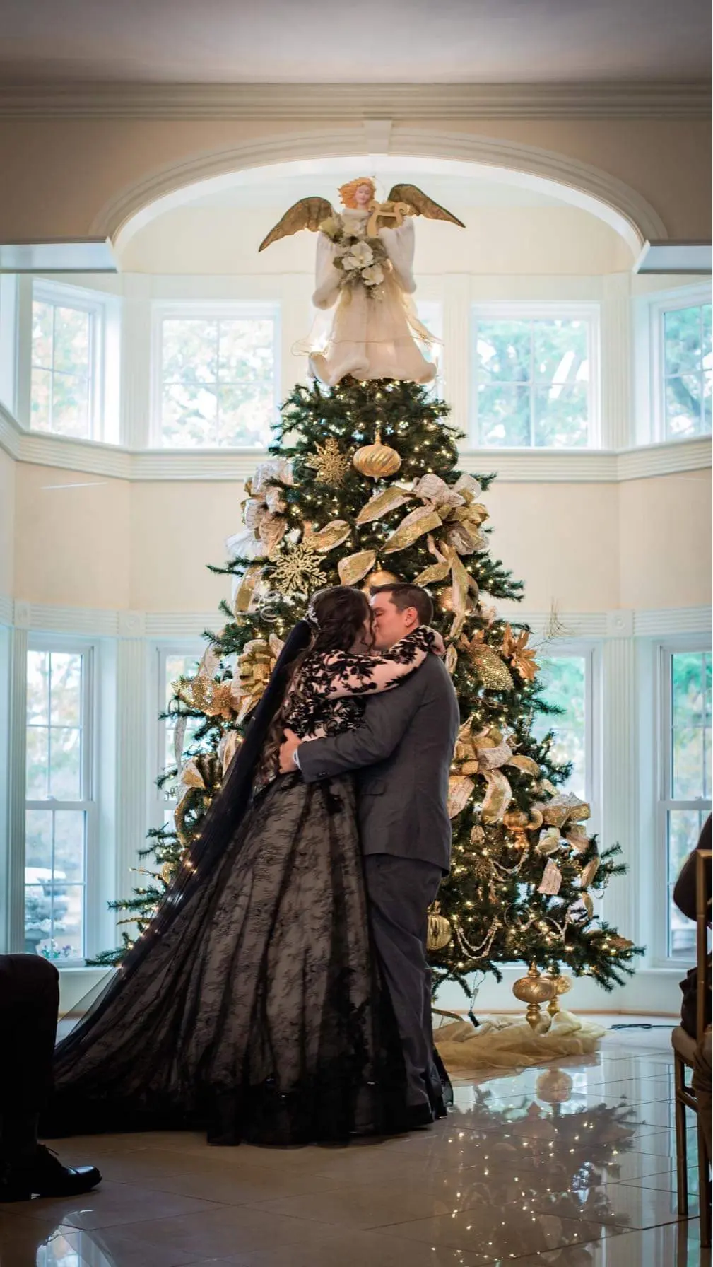 Bride Wearing Black Lace Ballgown Wedding Dress Called Zander By Sottero and Midgley Kissing Groom In Front Of A Christmas Tree