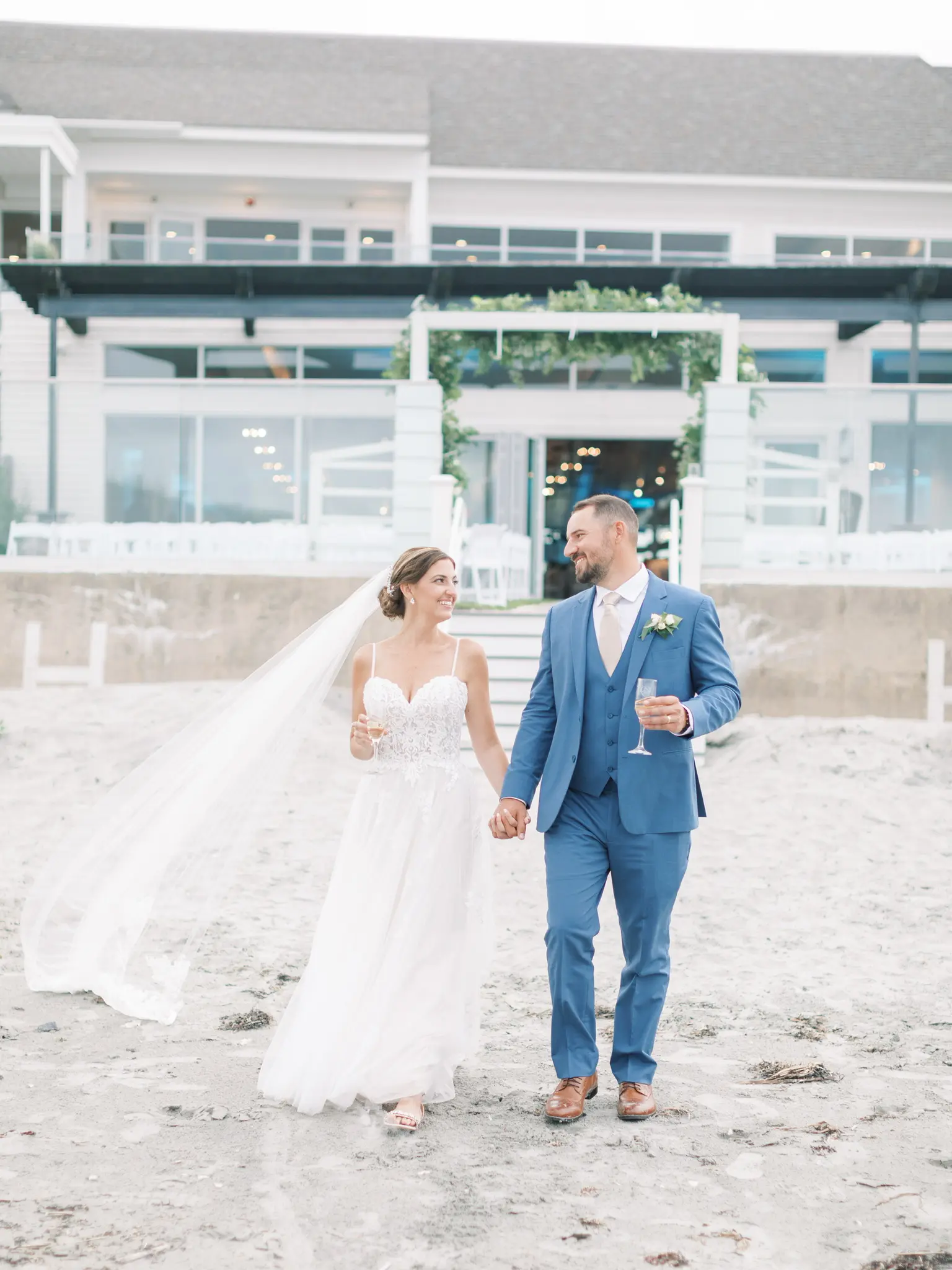 Bride Wearing Boho Sheath Wedding Dress Called Marisol By Rebecca Ingram Holding Hands With Groom On The Beach