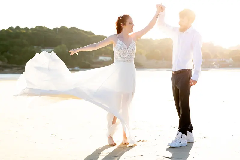 Bride Wearing Affordable Sheath Wedding Dress Called Lorraine By Rebecca Ingram Spinning On The Beach With The Groom
