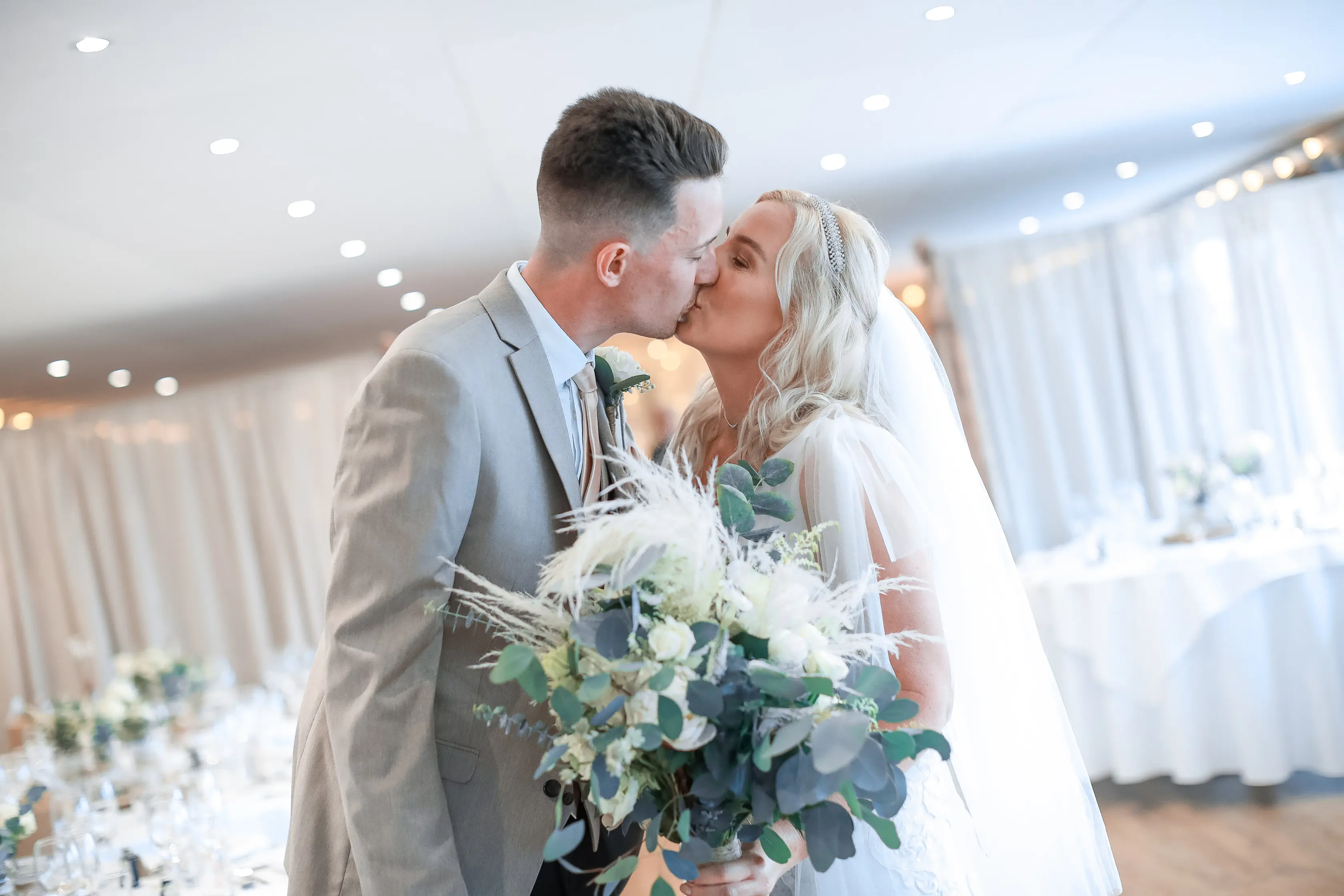 Newlyweds kissing and bride holding ivory bouquet.