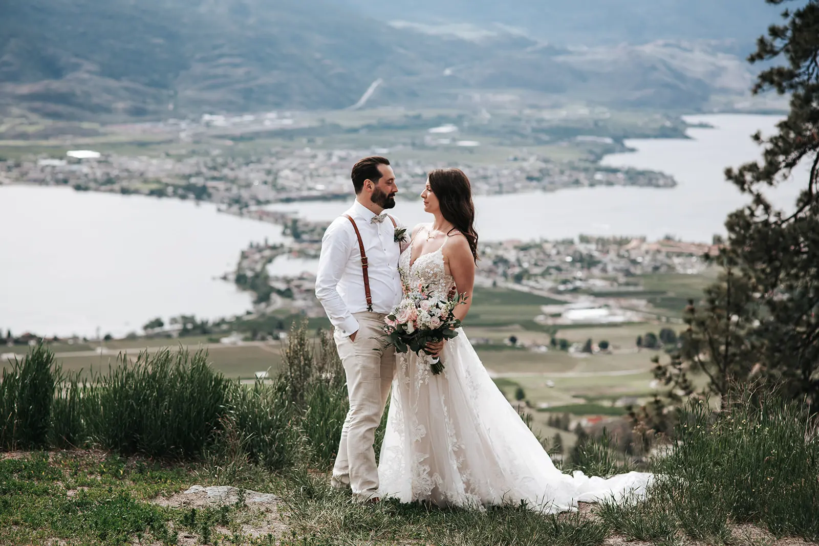 Bride Wearing Romantic Key Hole Back A-Line Wedding Dress Called Marlow By Maggie Sottero Holds Bouquet With Groom On A Mountain