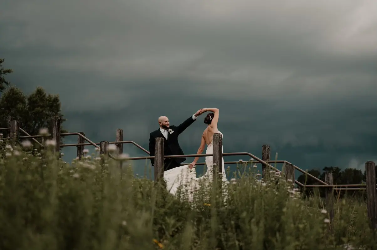Bride and groom dancing underneath dark grey clouds.