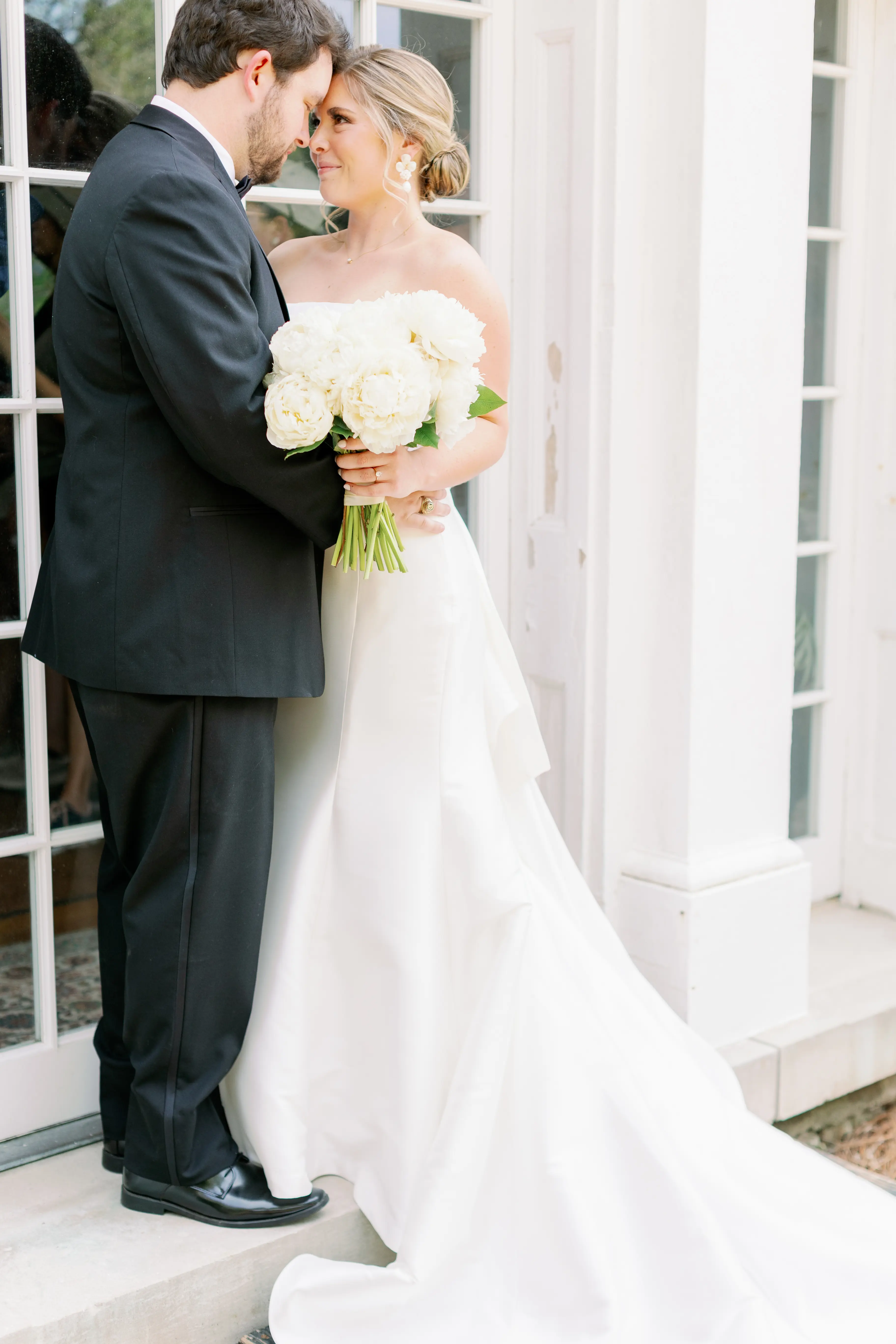 Bride with groom wearing strapless elegant mermaid wedding dress outdoors holding flower bouquet.