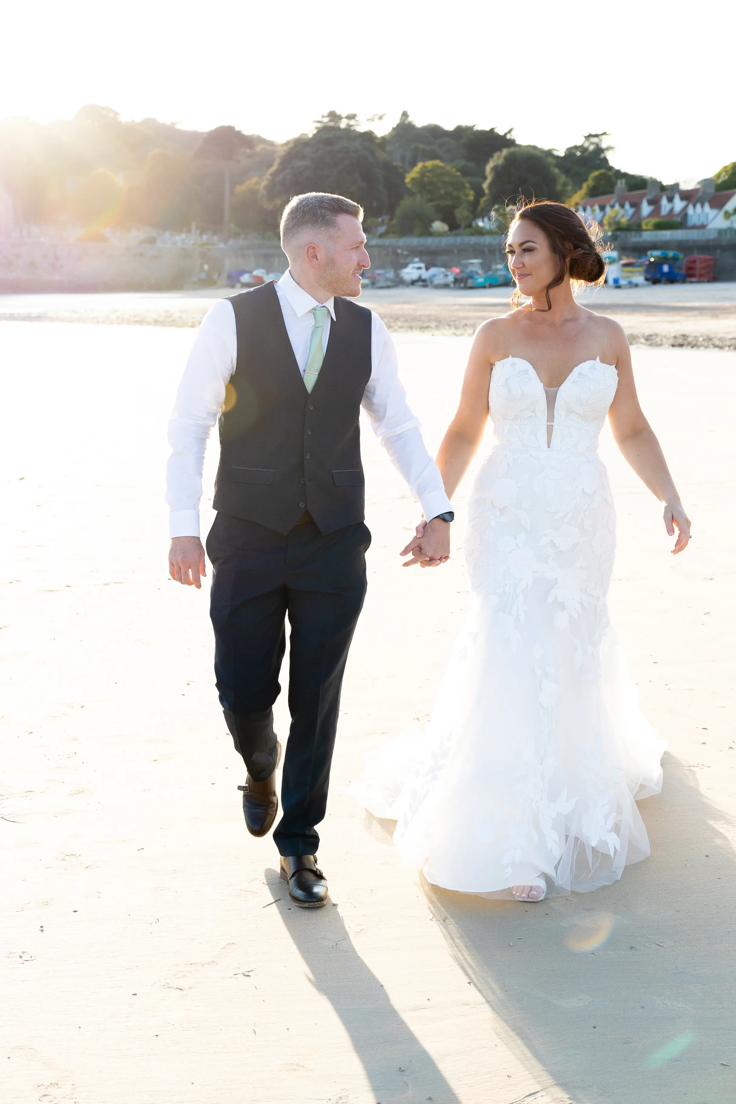Bride Wearing Lace Mermaid Wedding Dress Called Hattie By Rebecca Ingram Walking On The Beach With Groom