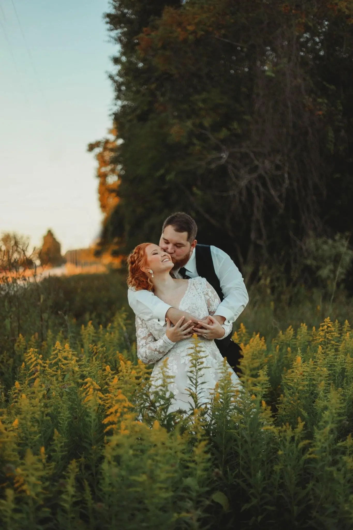Groom Kissing Bride In Loving Embrace While Standing In Nature. Bride Wearing Illusion Sleeve A-line Wedding Dress Called Raphael By Maggie Sottero