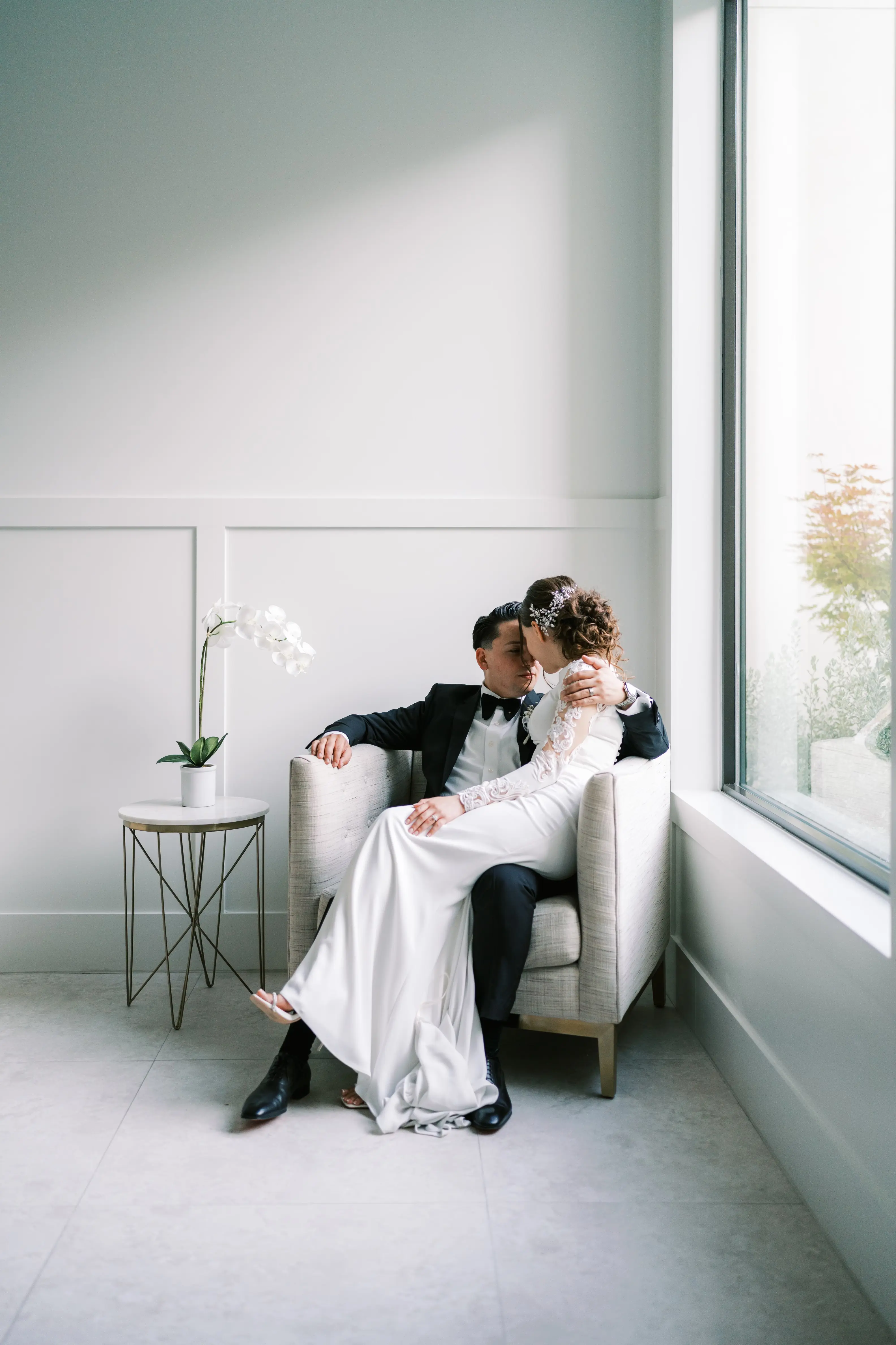 Bride Wearing Simple Long Sleeve Wedding Dress Called Bethany By Rebecca Ingram Sitting On Grooms Lap