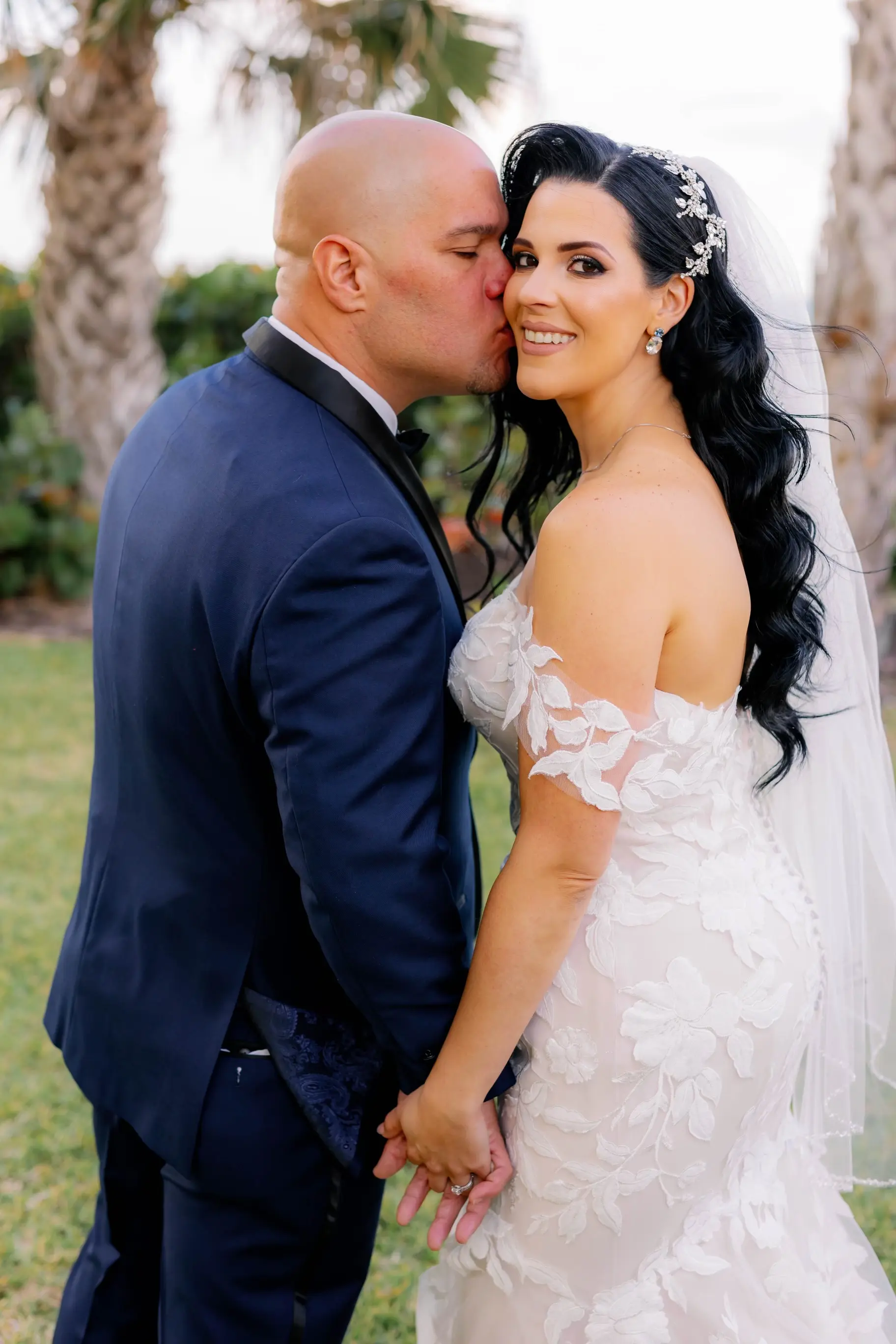 Bride Wearing Lace Mermaid Wedding Gown Called Hattie By Rebecca Ingram With The Groom Kissing Her Cheek