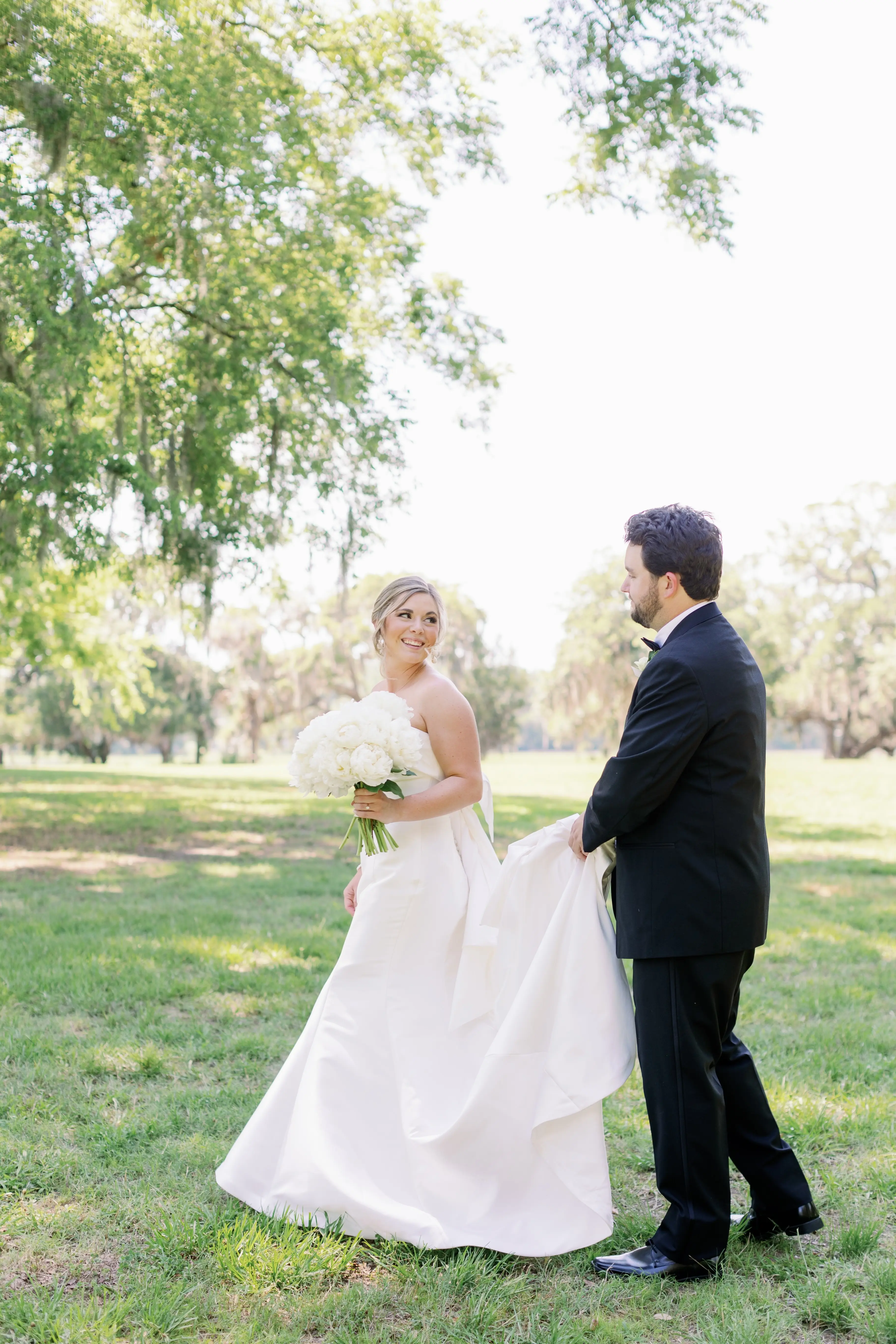 Bride with groom wearing strapless elegant mermaid wedding dress outdoors holding flower bouquet.