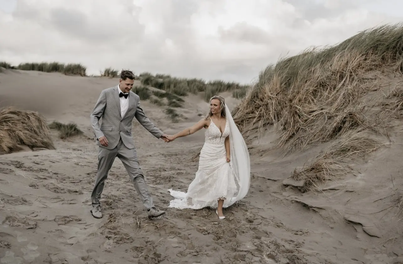 Bride Wearing Illusion Lace Back Wedding Dress Called Hamilton By Sottero And Midgley Walking With Groom On The Beach