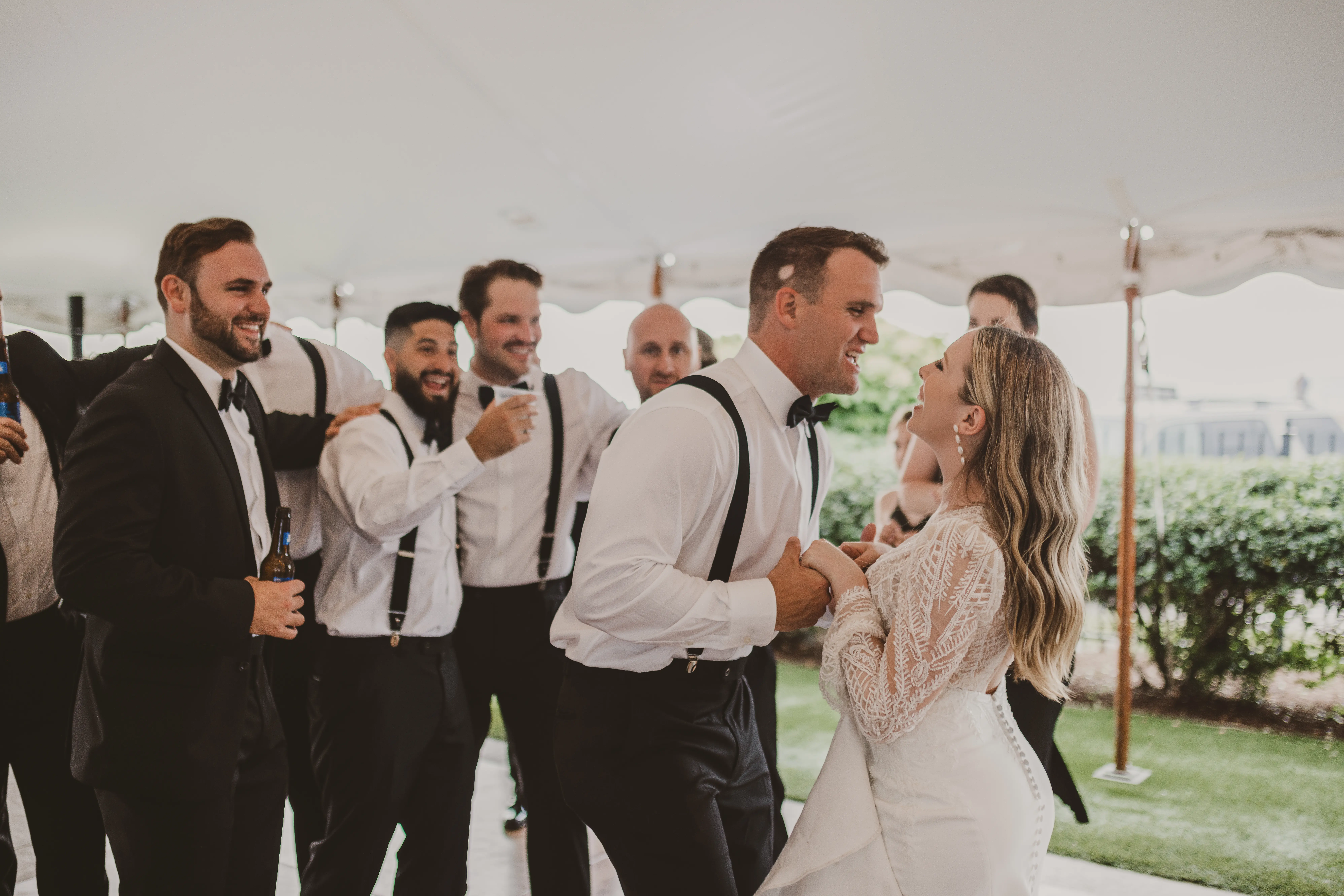 Bride and groom dancing under marquee with all the groomsmen smiling in background.