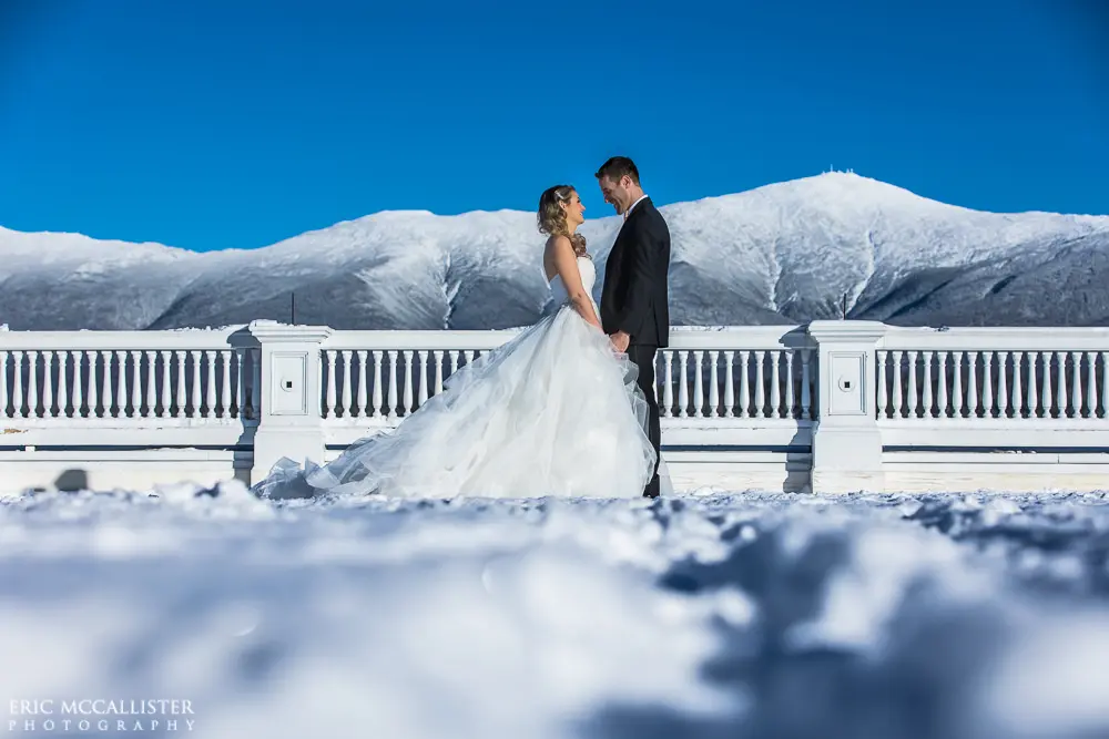 Bride with groom wearing strapless ballgown tulle wedding dress with sweetheart neckline outdoors in front of mountains.
