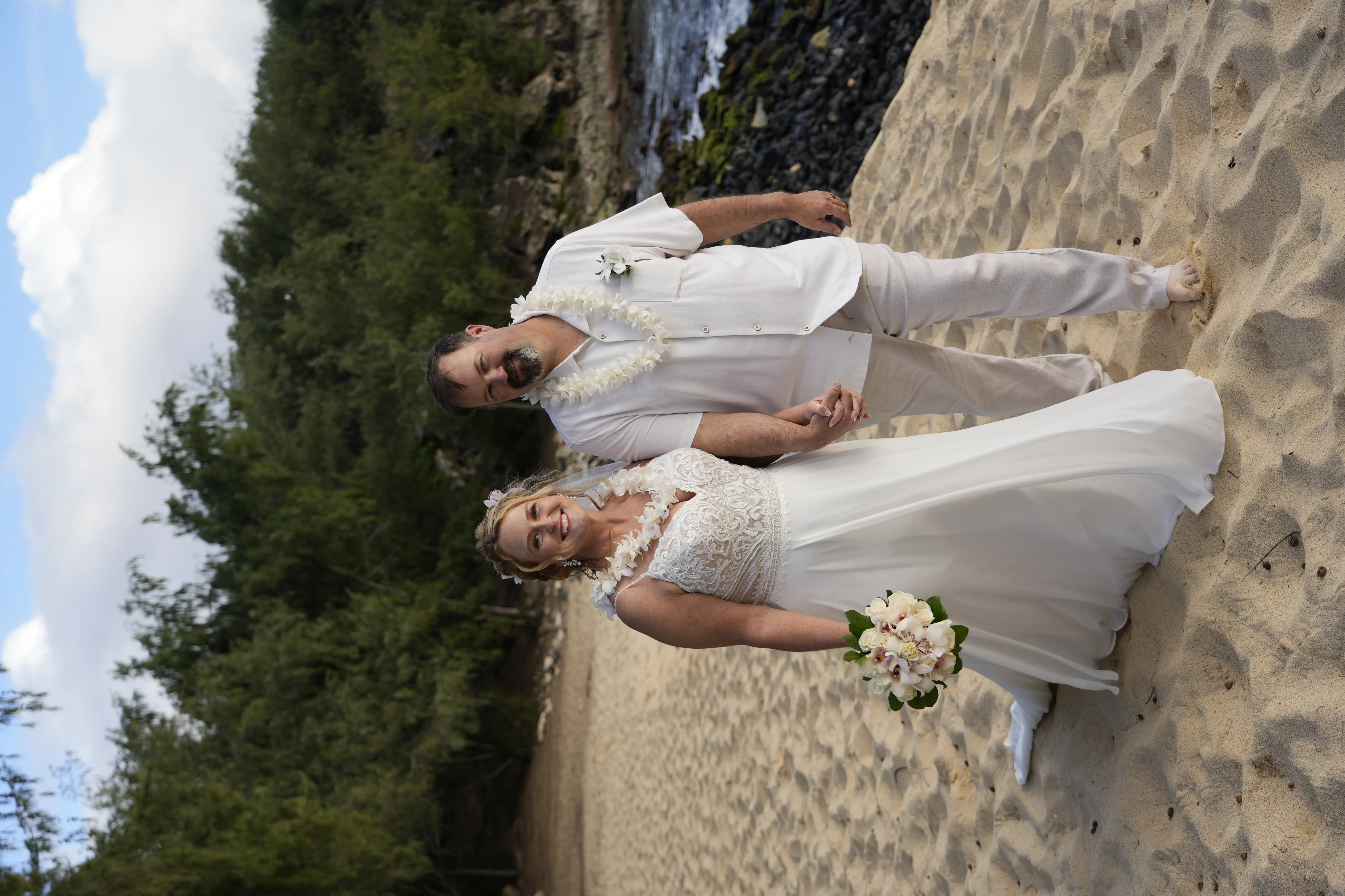 Bride wearing Lorraine wedding dress by Rebecca Ingram holding hands on the beach with her husband