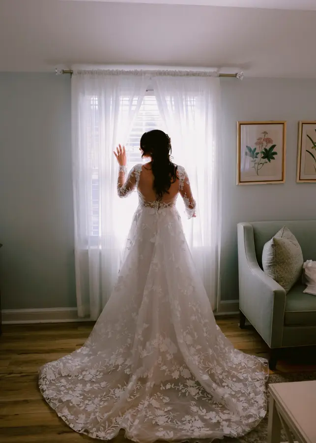 Bride Wearing Lace Long Sleeve Aline Wedding Dress Called Winter By Maggie Sottero Standing Next To A Window