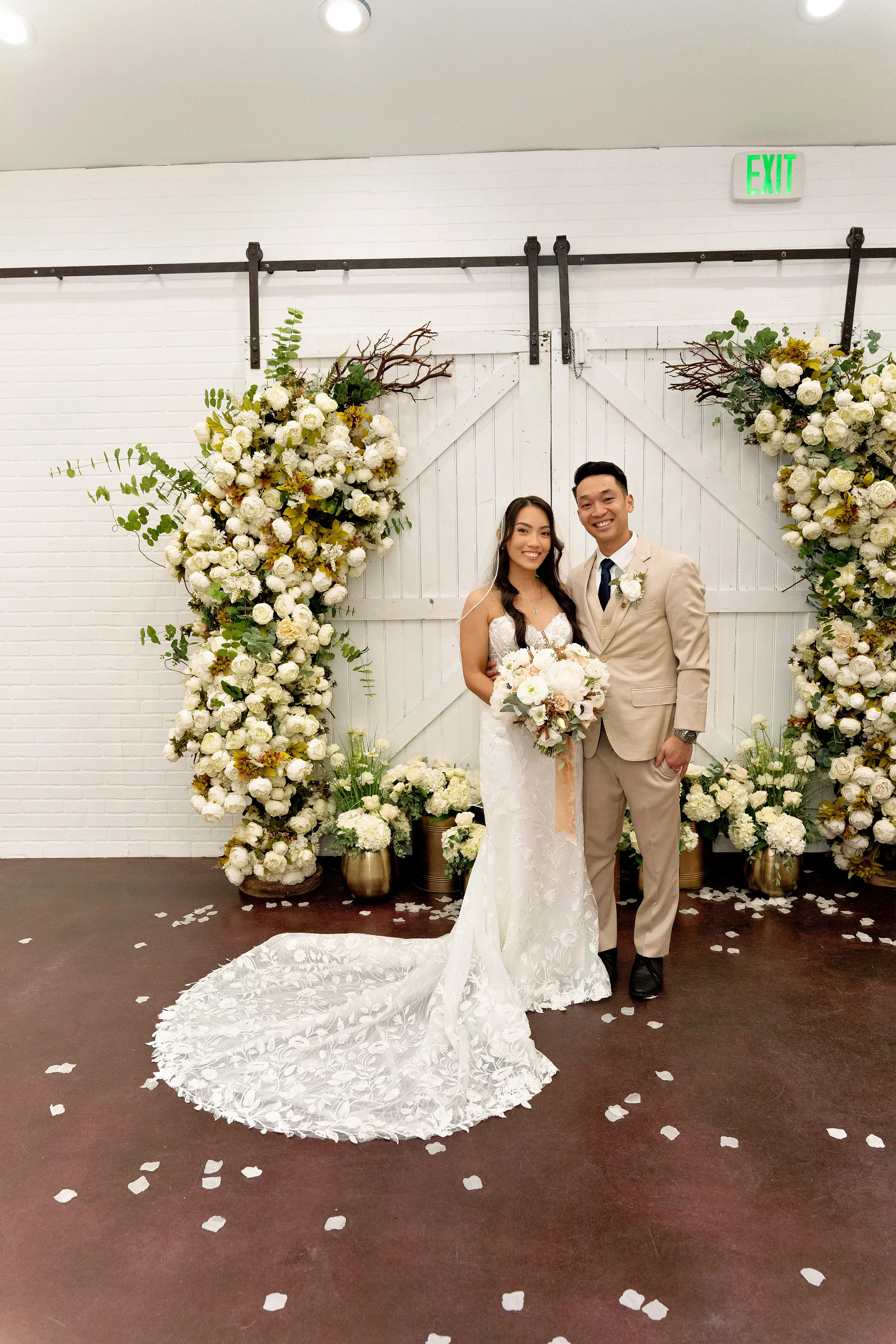 Bride Wearing Lace Fit And Flare Wedding Dress Called Fairchild By Maggie Sottero With Groom Next To A Flower Arch
