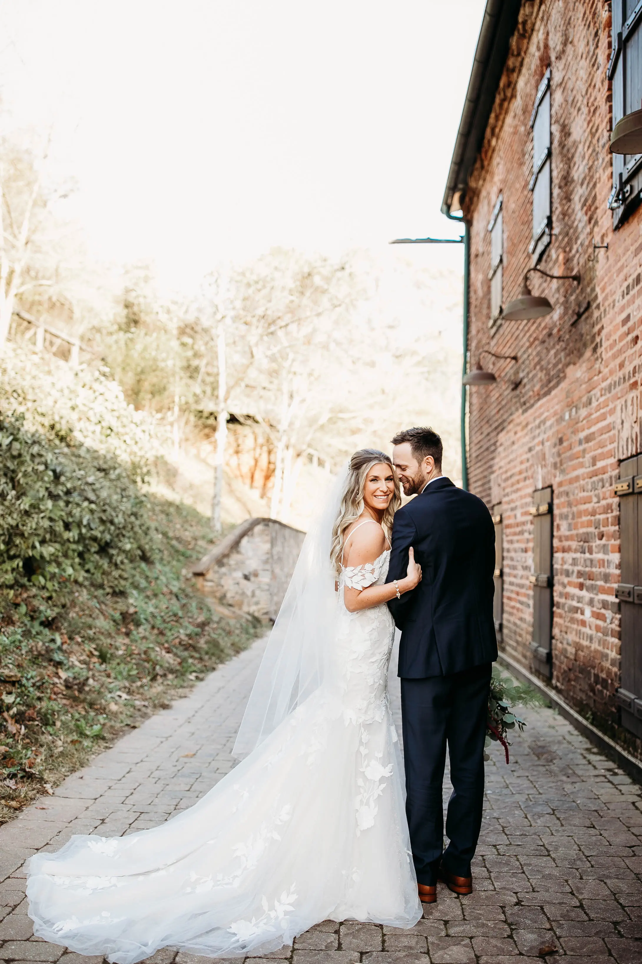 Bride And Groom Standing Together. Bride Wearing Mermaid Wedding Dress With Oversized Lace Called Hattie By Rebecca Ingram