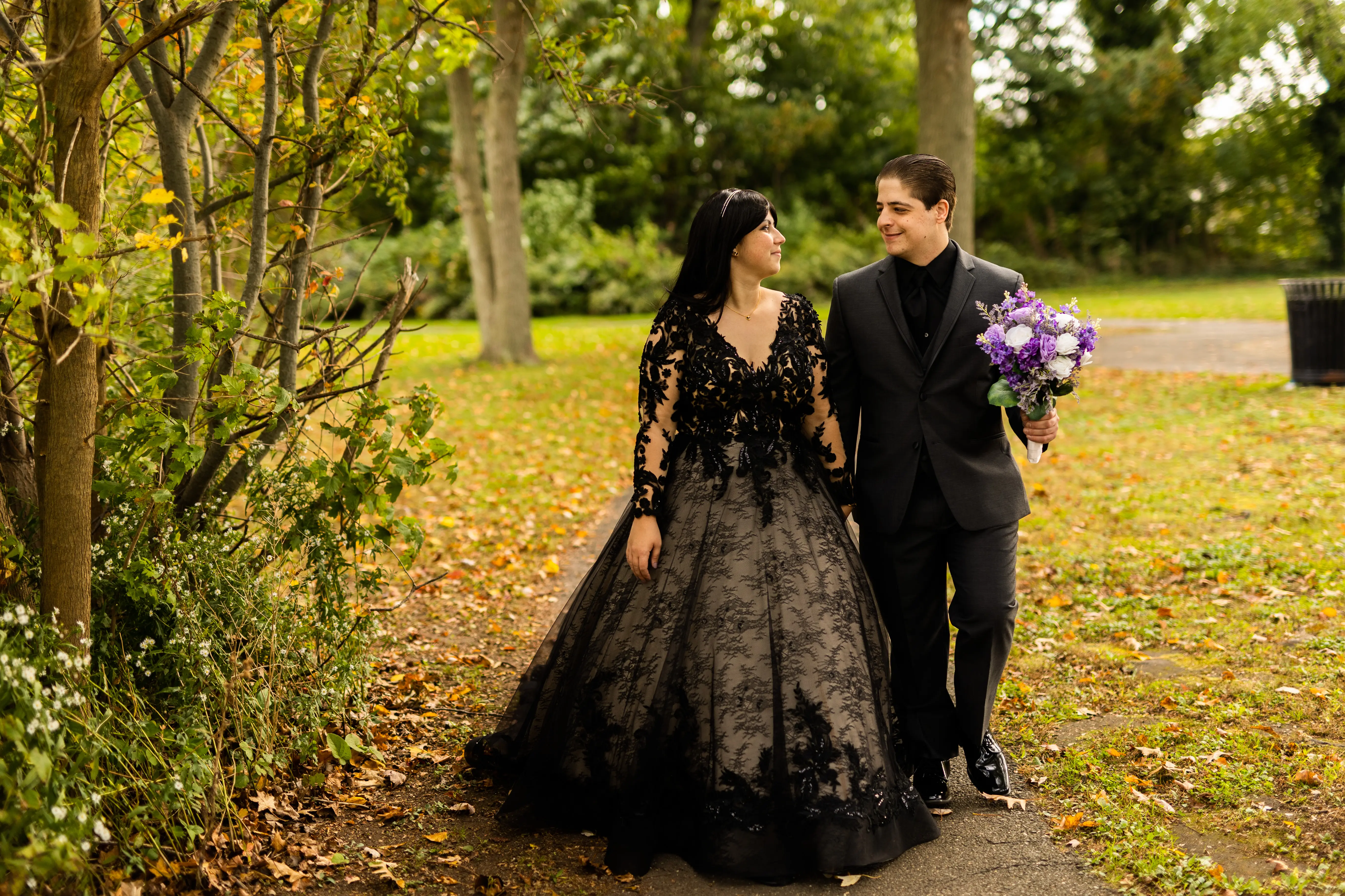 Bride in a Field with Groom Wearing Long Sleeve Black Lace Ballgown Wedding Dress Holding Bridal Bouquet.