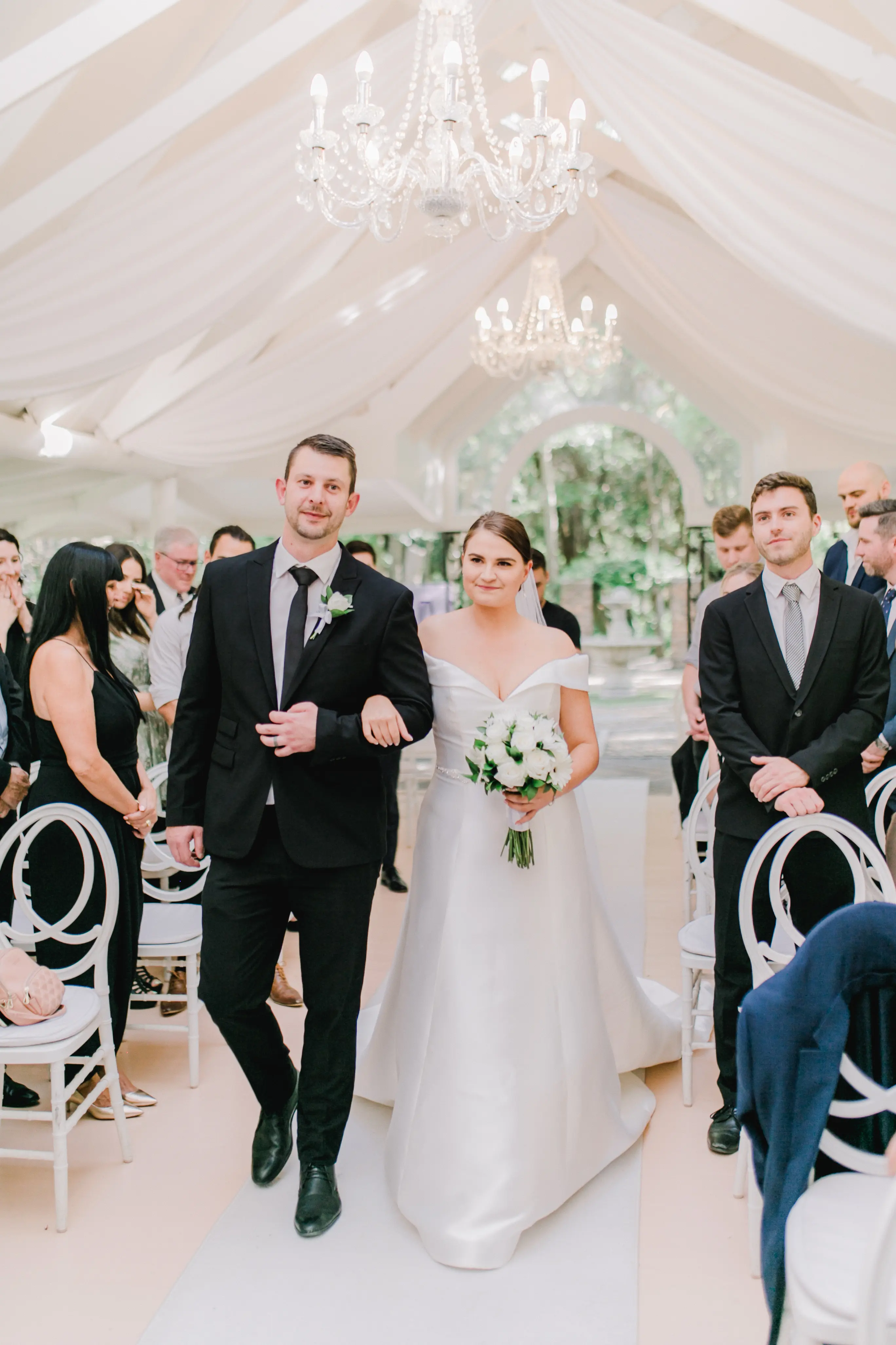 Bride Wearing Off-The-Shoulder A-Line Wedding Dress Called Coral By Rebecca Ingram Walking Down The Aisle
