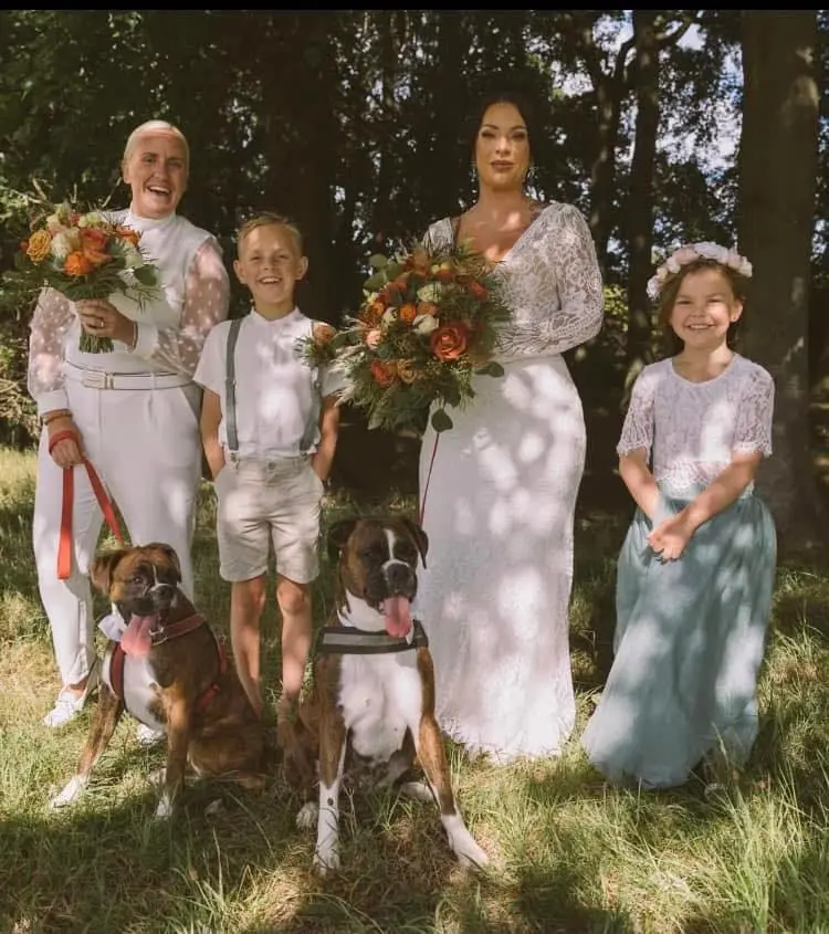LGBTQ+ Brides At Beach Wedding With Bride In Open Back Long Sleeve Wedding Dress Called Drita By Sottero And Midgley With Kids And Dogs