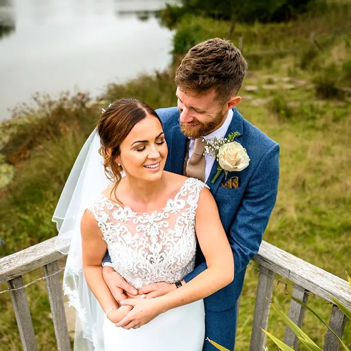 Bride and groom hugging by a lake.