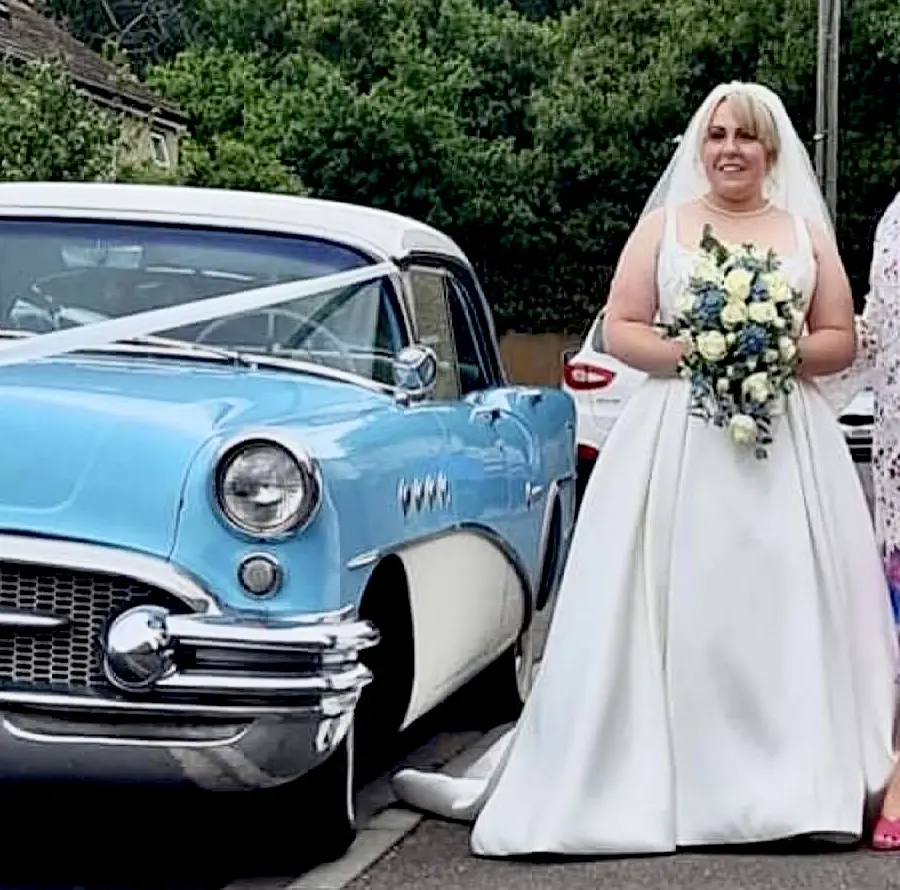 Bride standing by vintage blue and ivory car wearing dress called Selena.