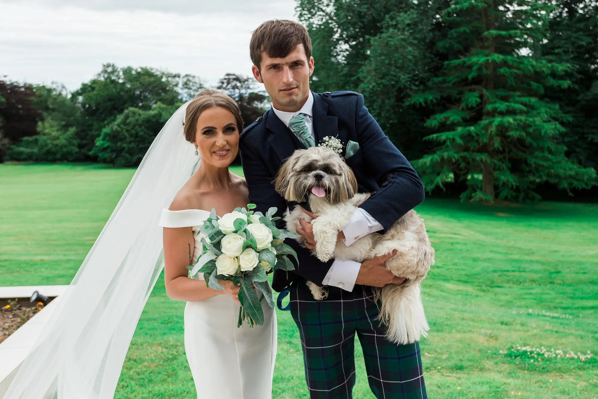 Bride wearing wedding dress called Josie with groom holding a cute puppy dog.