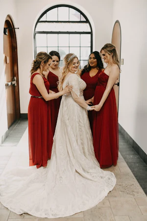 Bride wearing wedding dress called Roxanne with bridesmaids in red.