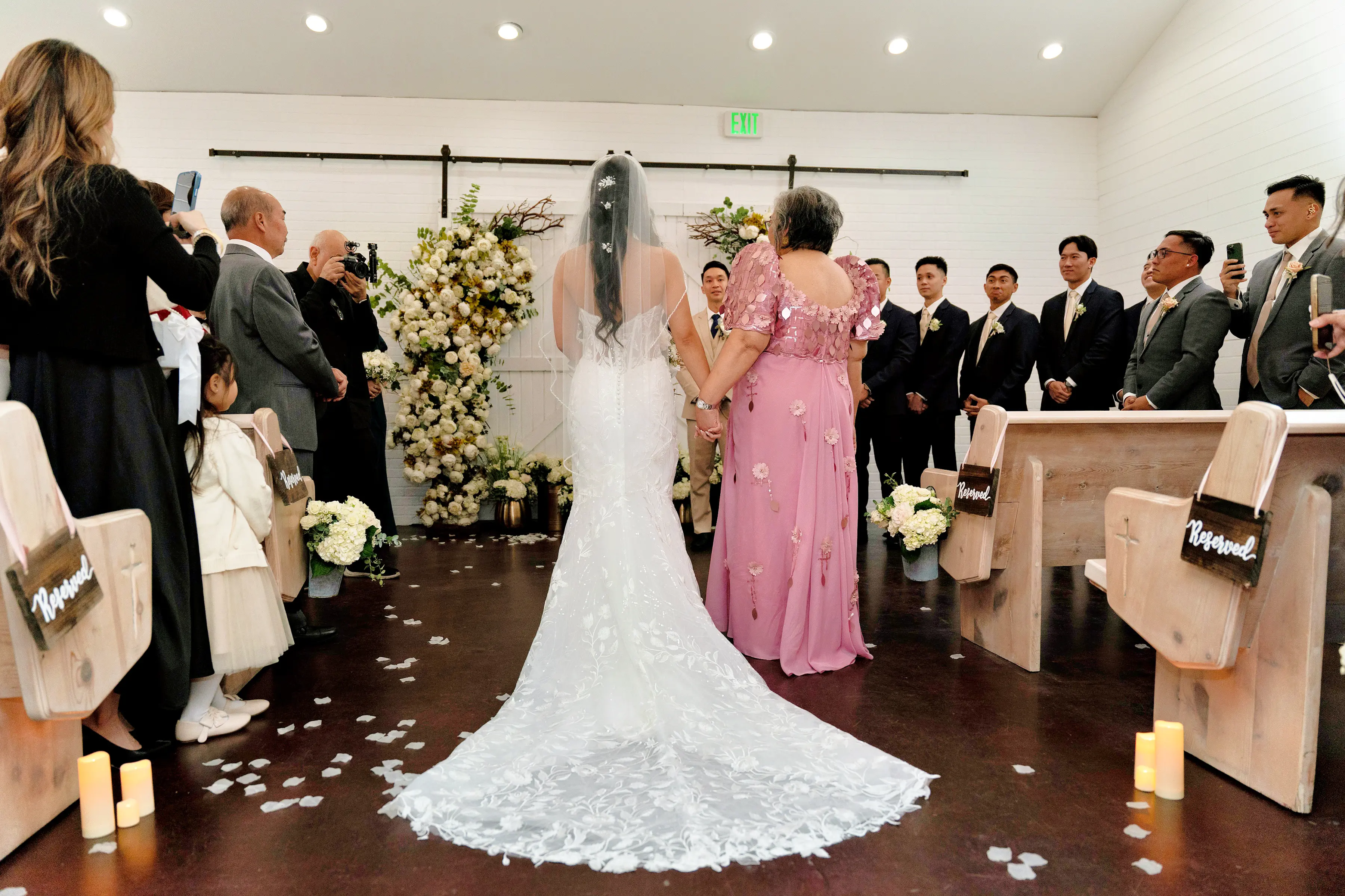 Bride Wearing Lace Fit And Flare Wedding Dress Called Fairchild By Maggie Sottero Walking Down The Aisle With Her Mom In A Floral Pink Dress