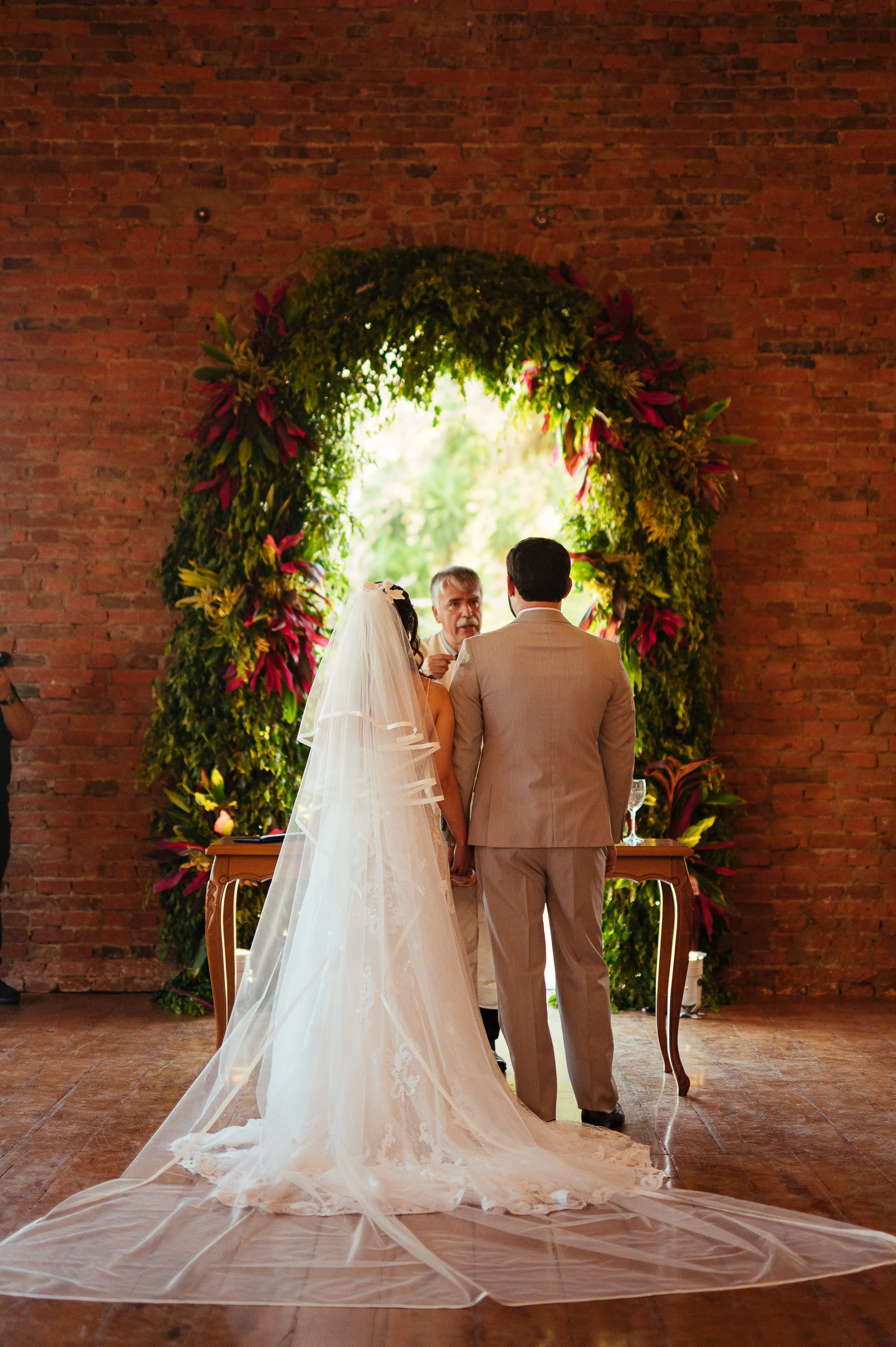 Bride Wearing Flattering Full Lace Wedding Dress Called Tuscany Lane By Maggie Sottero Standing With Groom In Wedding Ceremony Under Green Arch